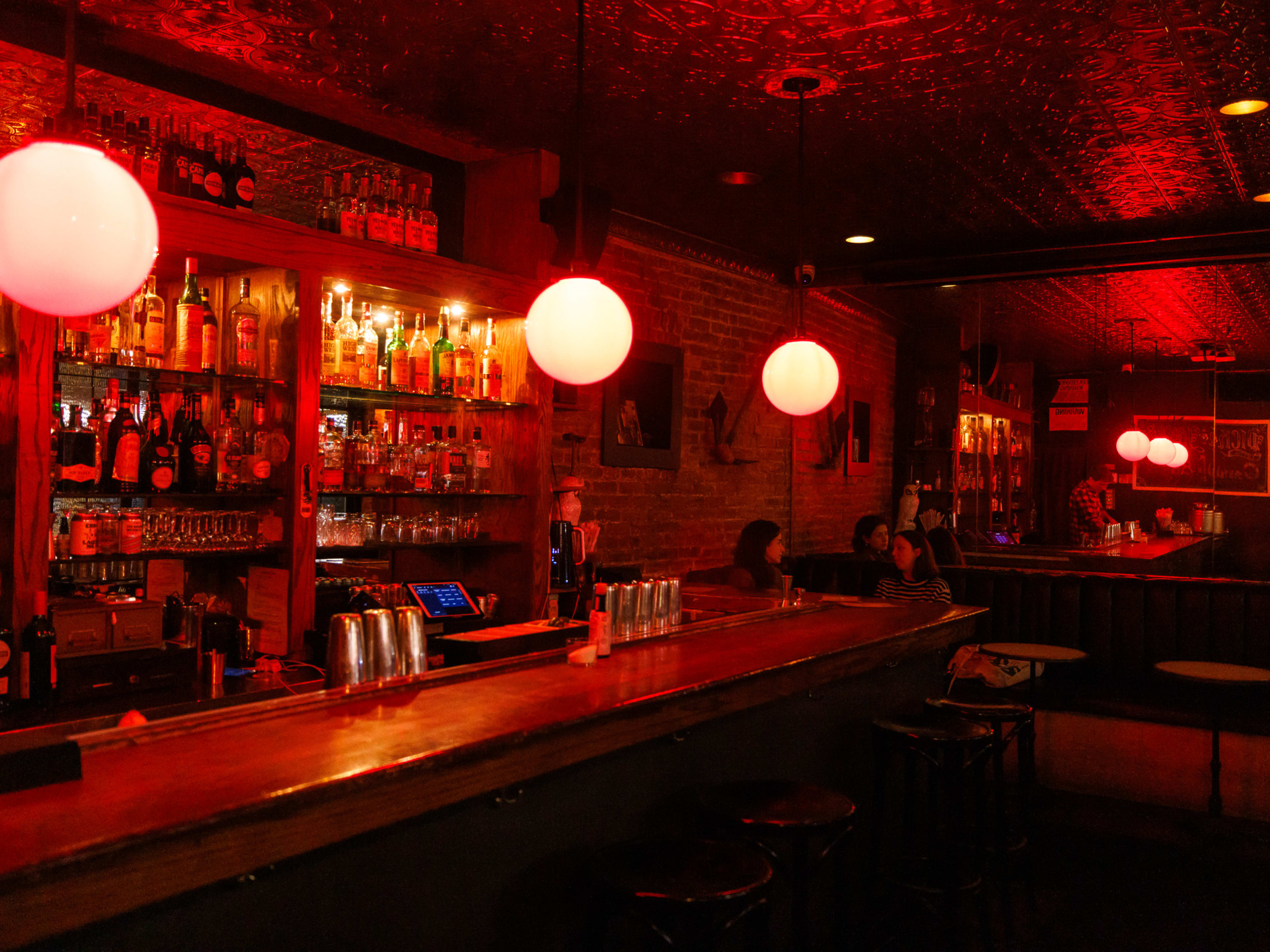 Dick & Jane's interiors with red dim lighting, large orb lights above the bar, bar seating in the front and booth seating in the back