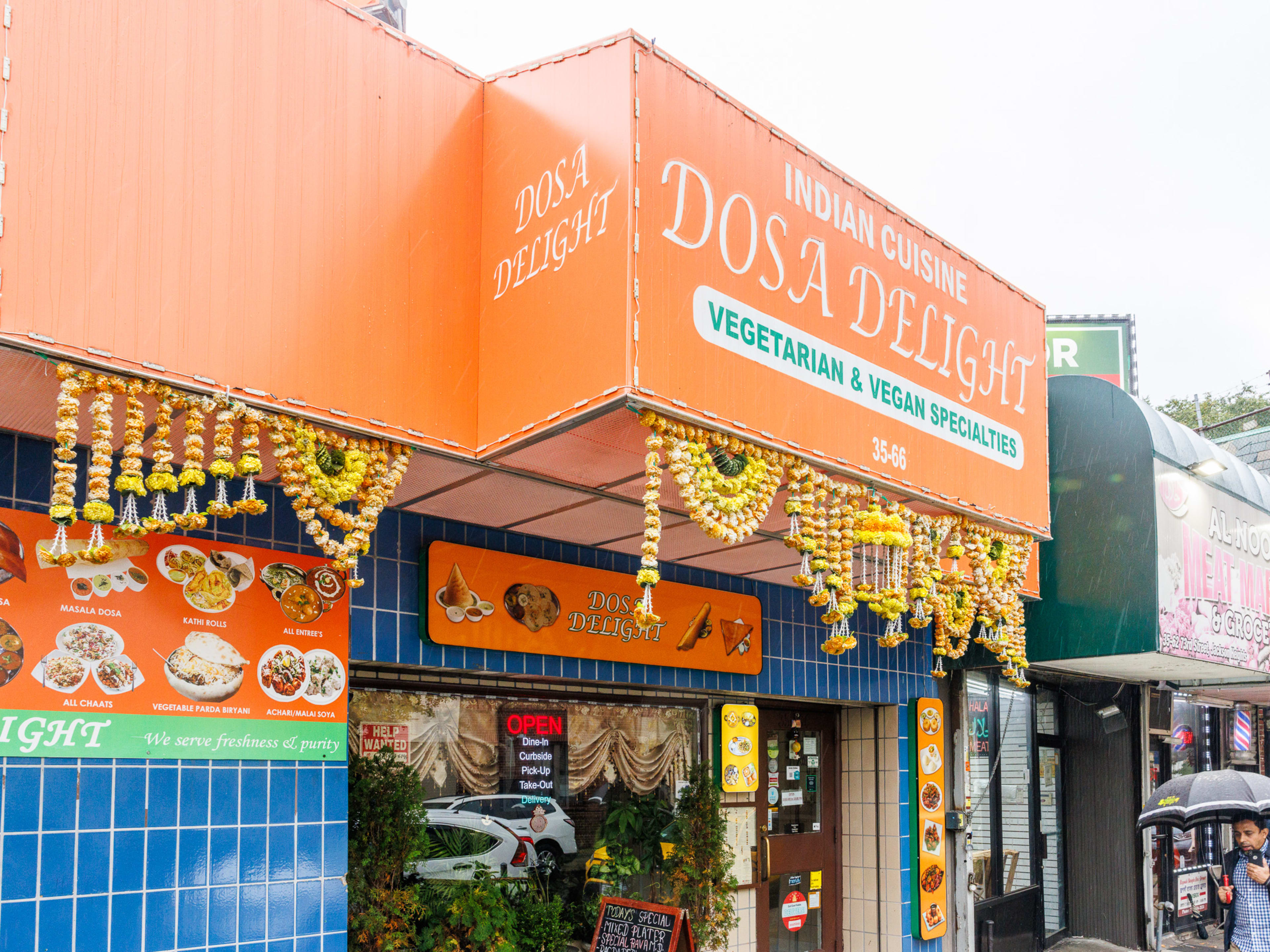 Dosa Delight blue tile exterior with large colorful restaurant awning with flowers hanging off it