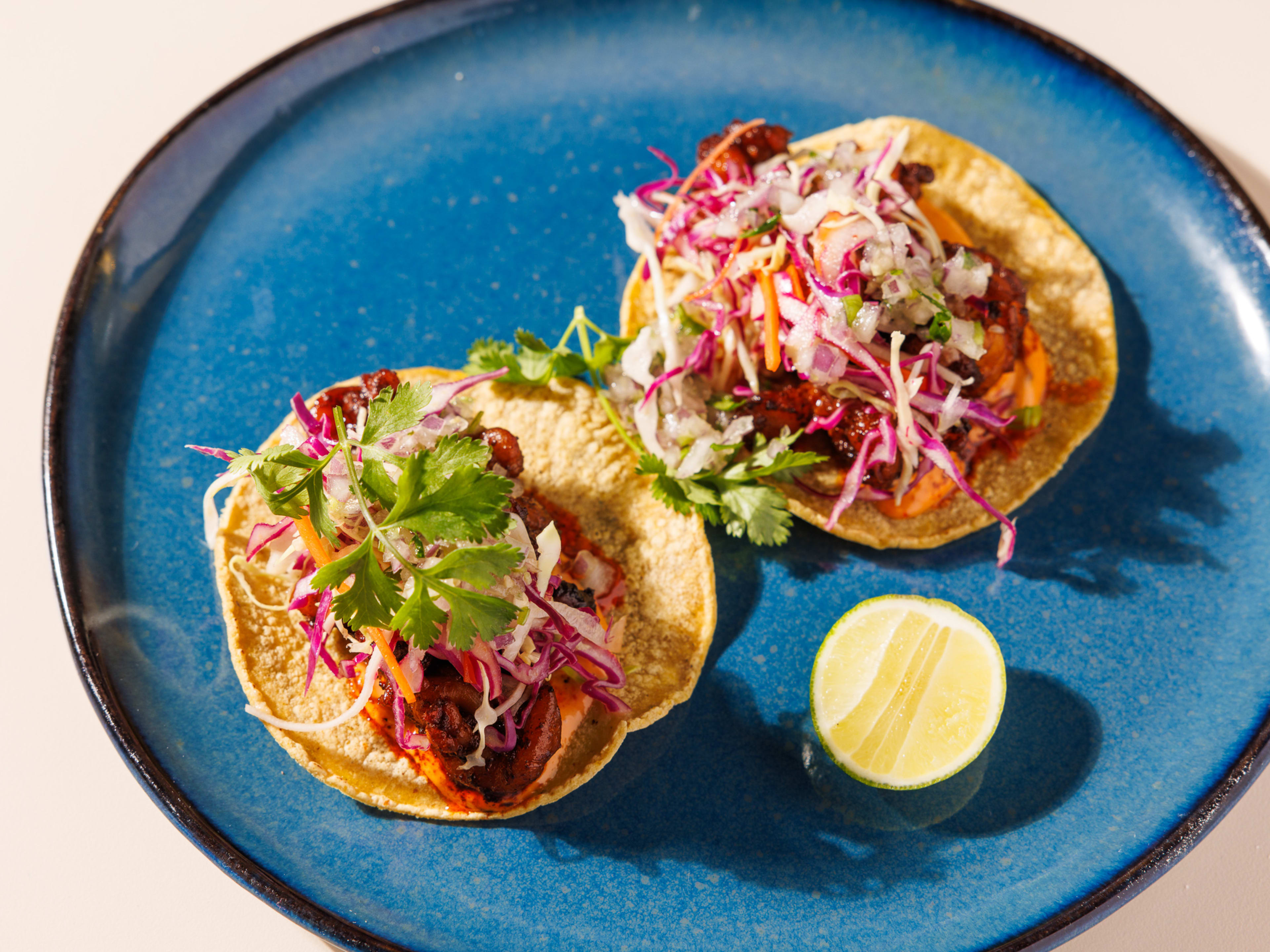 Two shrimp tacos topped with cabbage slaw on a blue plate.