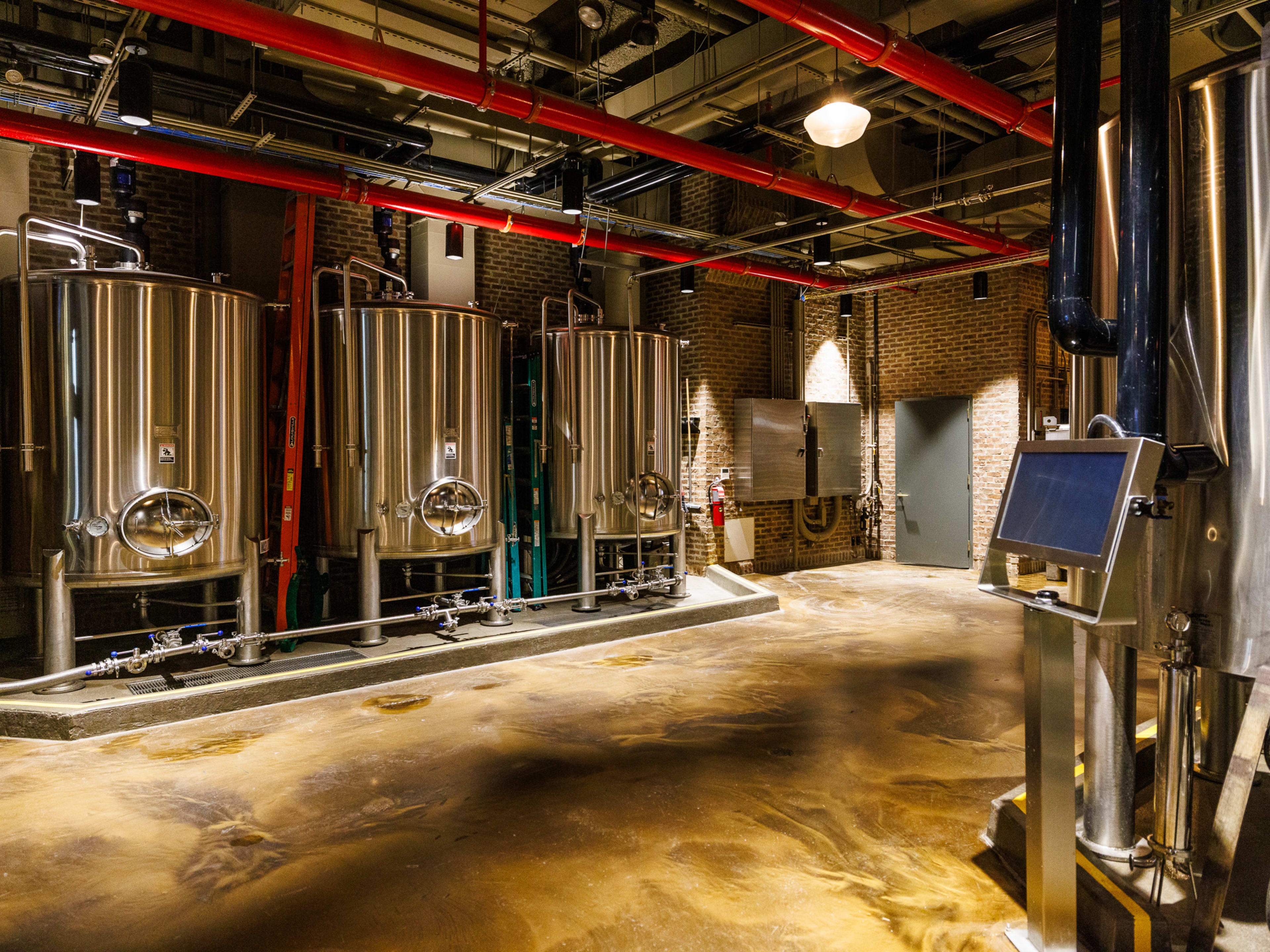 Great Jones Distilling Co. interiors with three distiller machines in a room with brick walls and red pipes on the ceiling