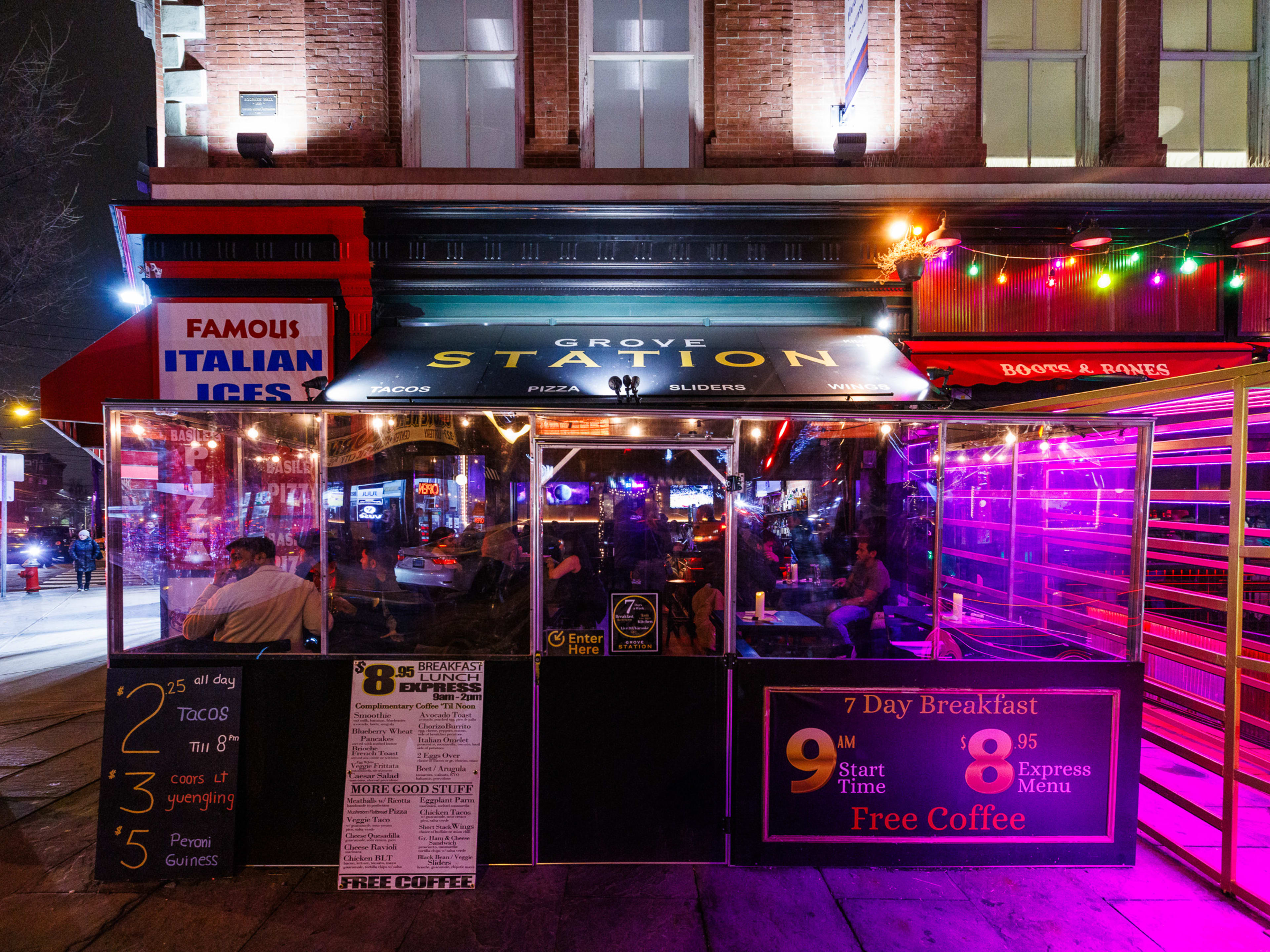 Grove Corner Bar exteriors at night with purple lighting, an enclosed outdoor seating area out front on the sidewalk, and colorful sting lights hanging next door