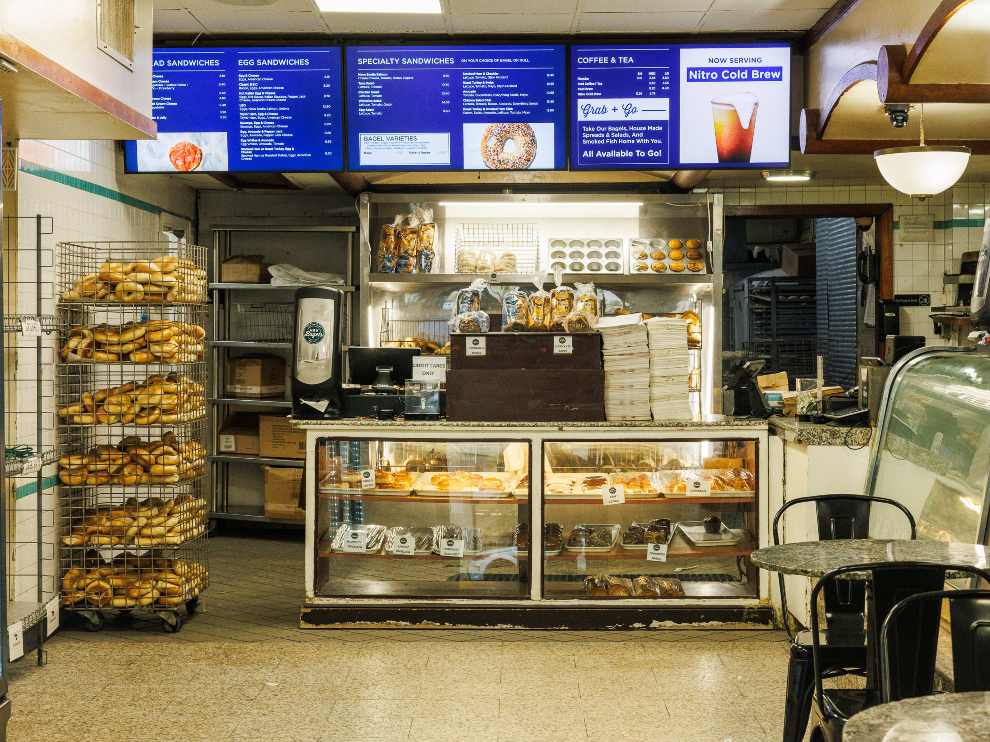 H&H Bagels interior with bagel display shelves and a menu on tvs