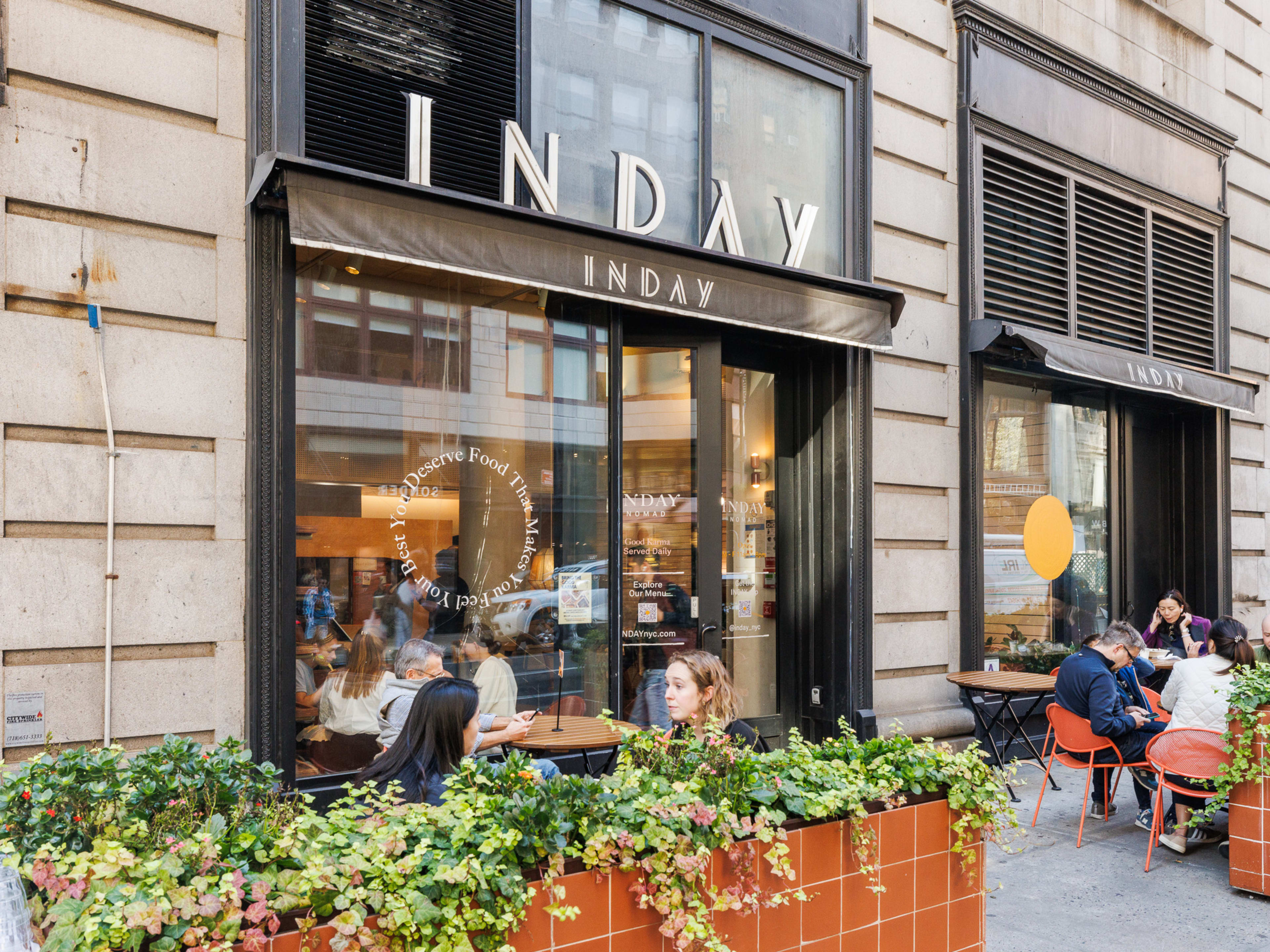 INDAY exterior with people sitting at outdoor tables surrounded by plants