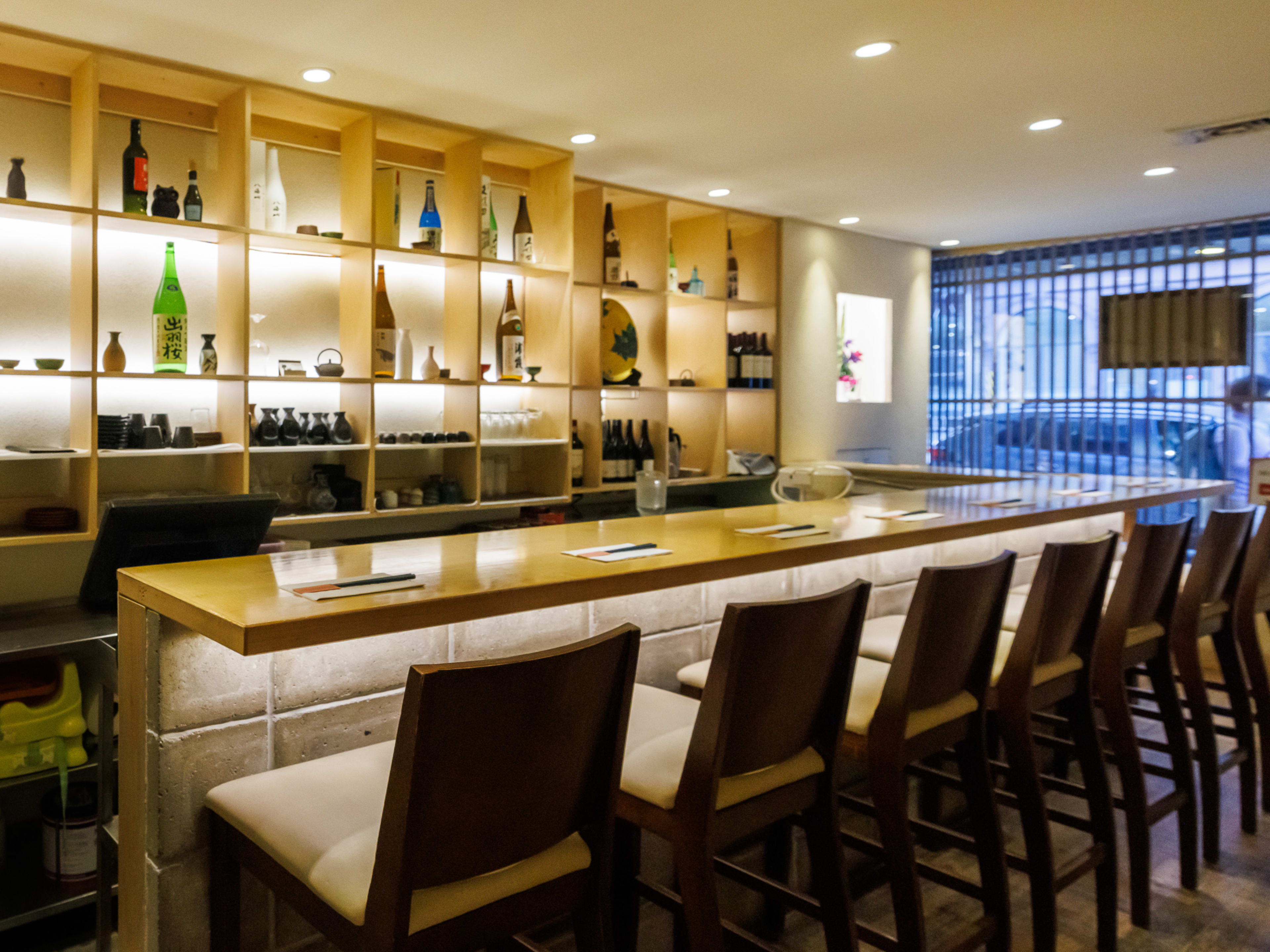 Ise interior with counter seating and a wall filled with alcohol bottles behind the bar