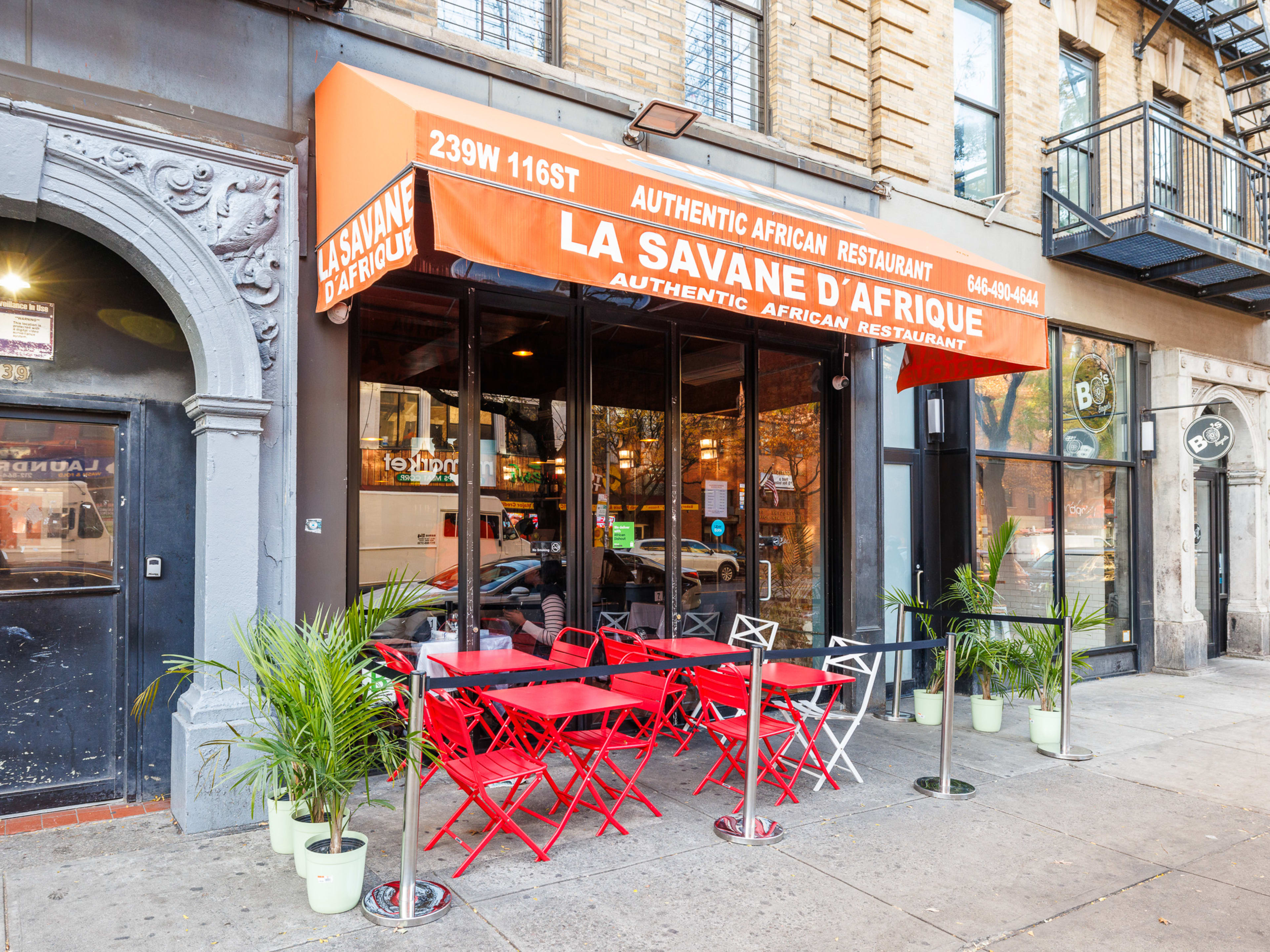 La Savane exterior with a large awning and four outdoor tables on the sidewalk sectioned off with rope and potted plants