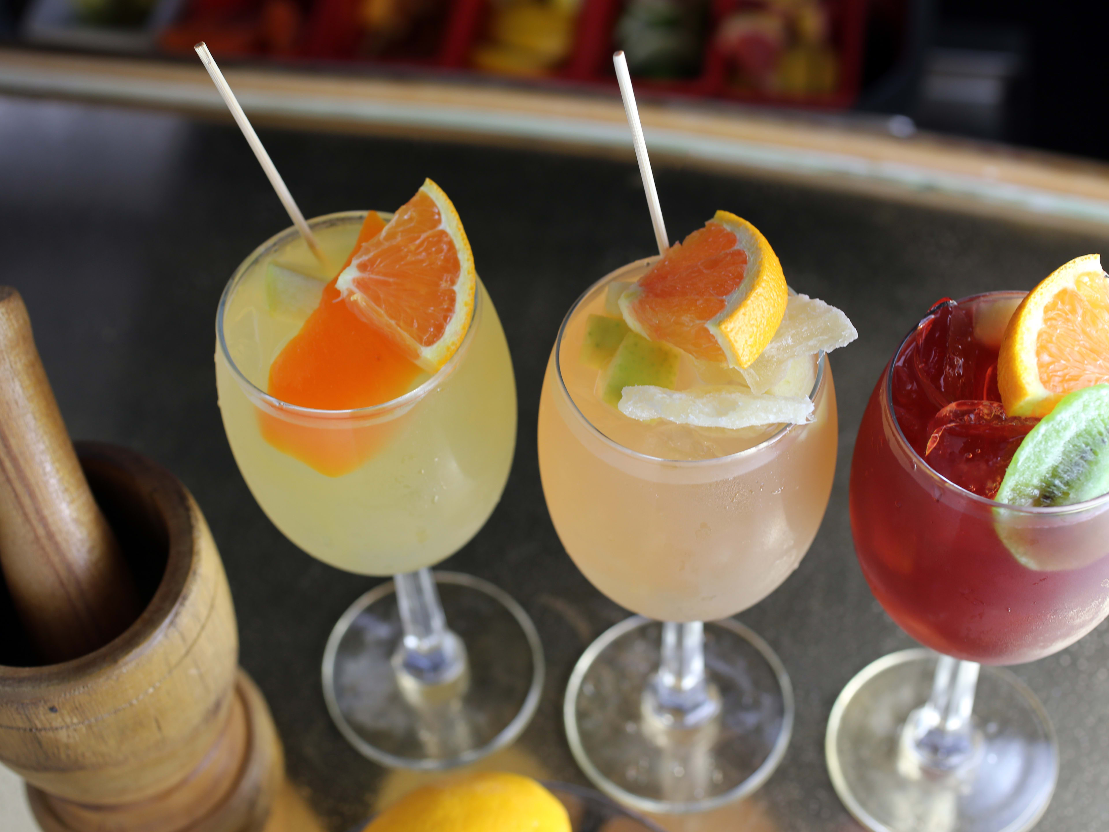 Three drinks lined up at the bar with multiple pieces of fruit in each glass