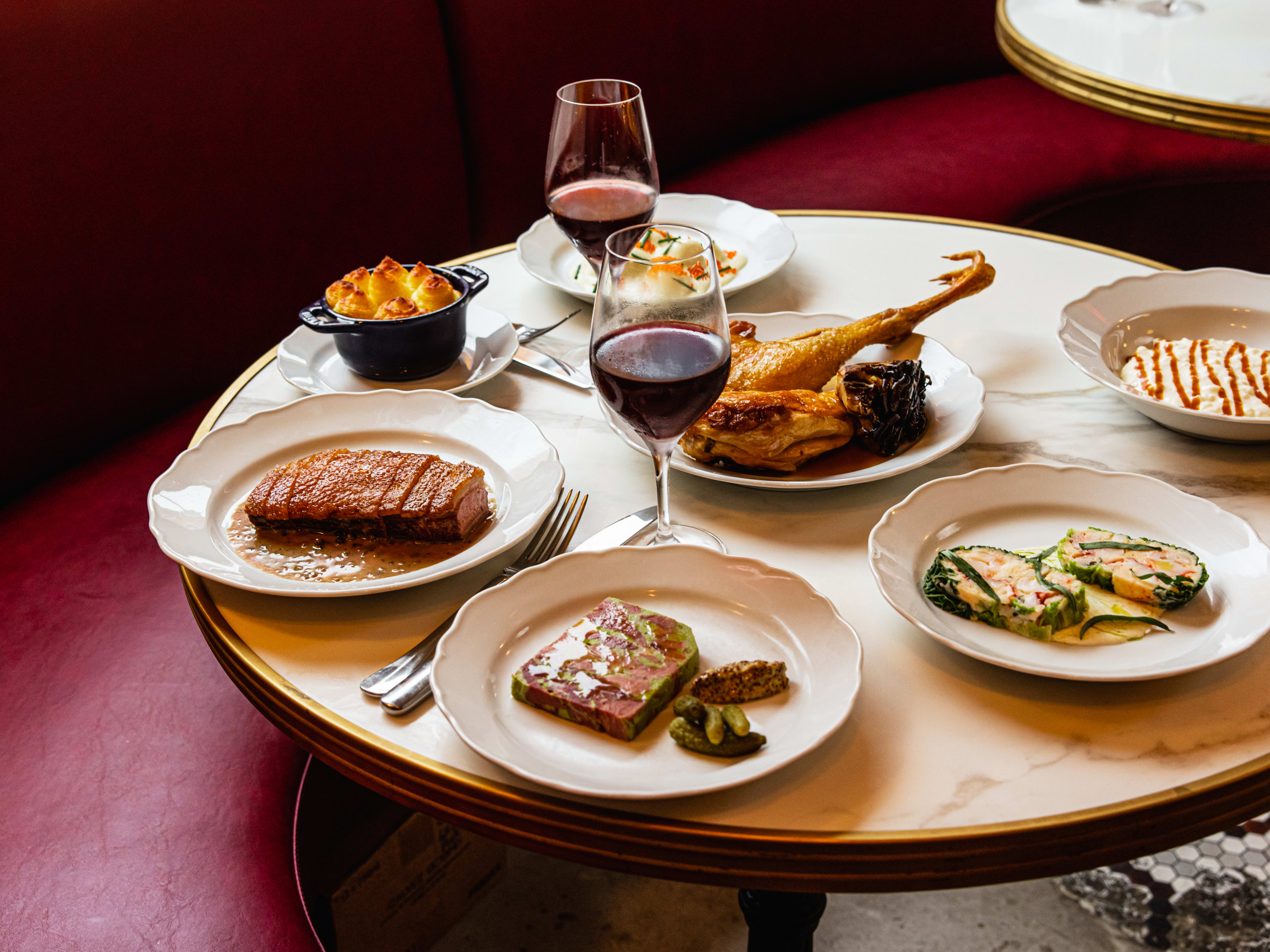 A spread of French food and wine on a marble table next to a red banquette.