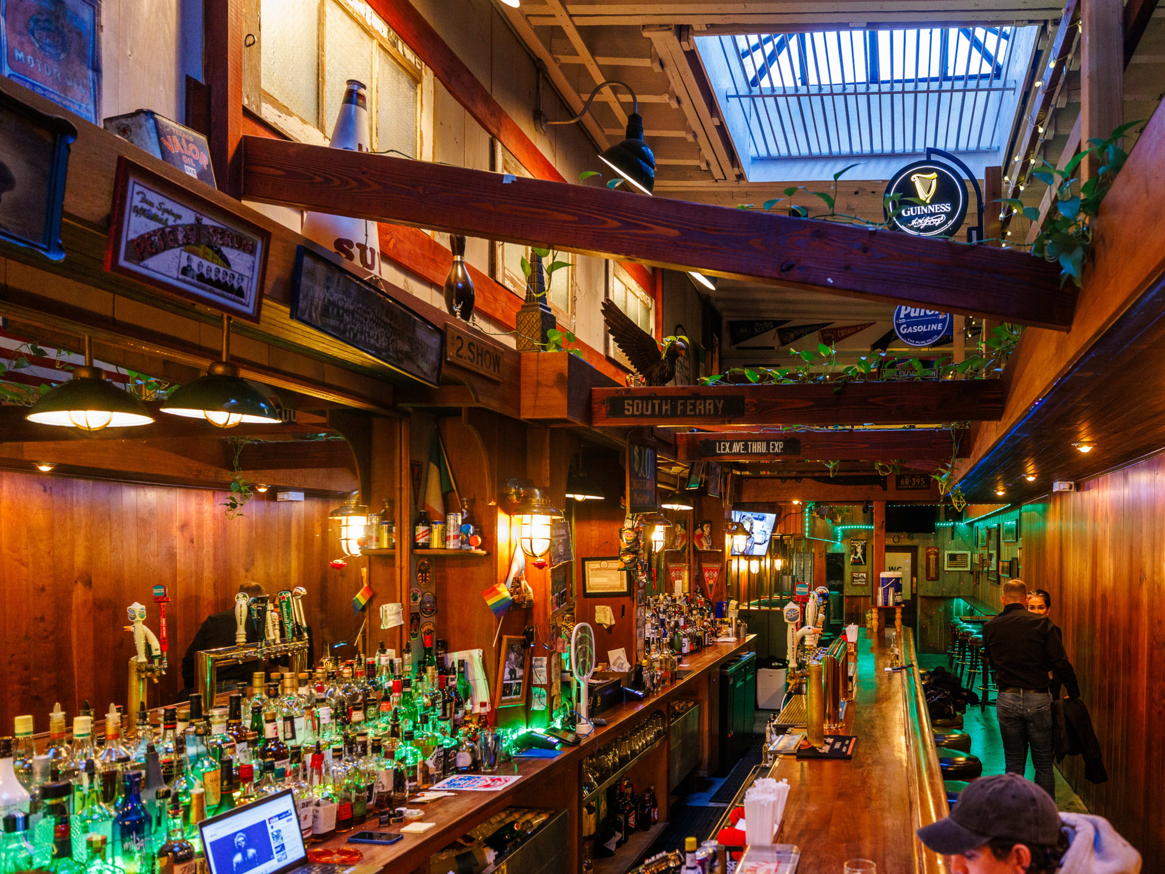 Local 138 interiors with green lighting, wood paneled walls, a long wooden bar with stool seating, and a skylight in the middle of the high ceiling.