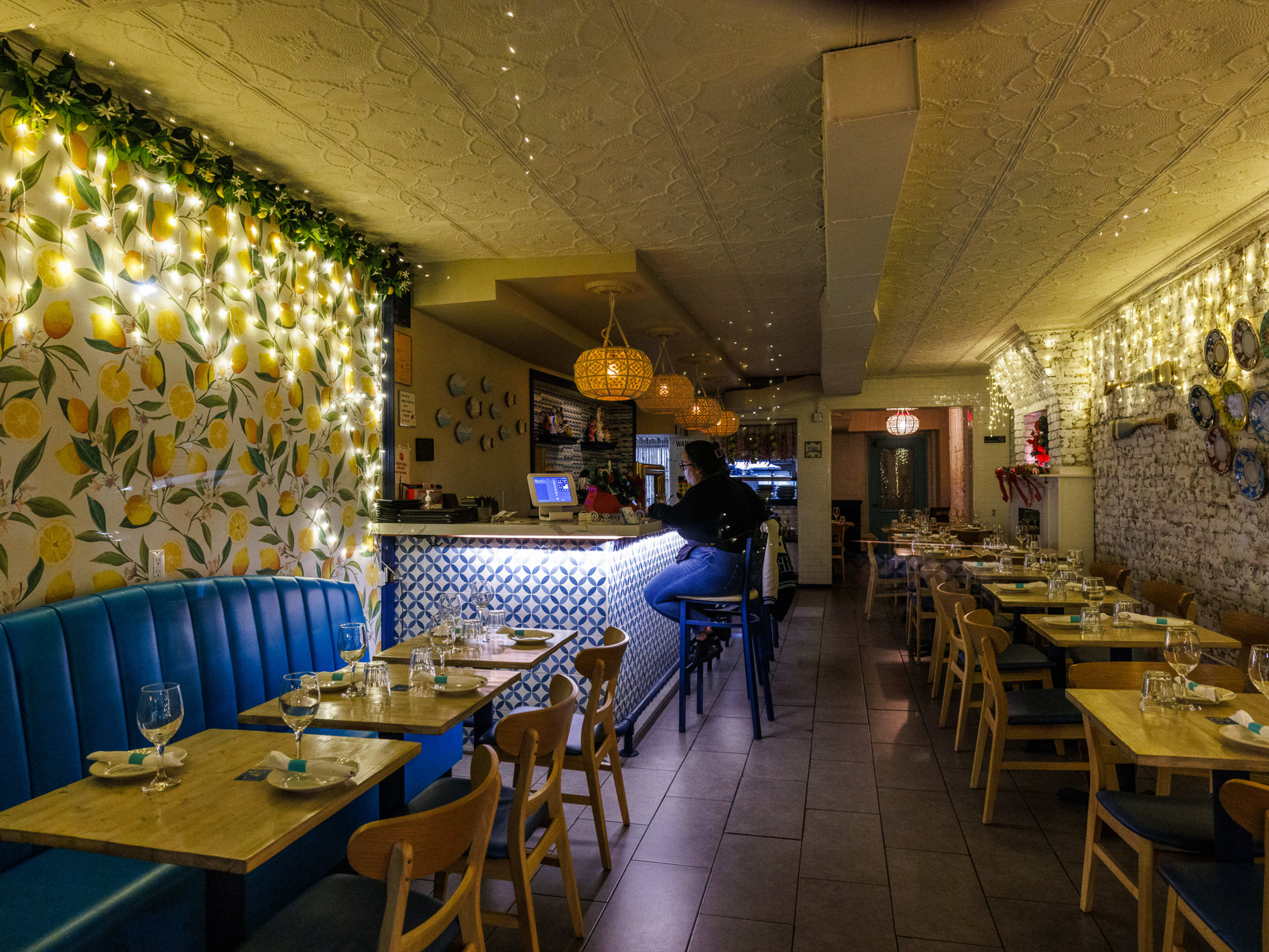 Mama Capri interior with blue booth seating, lemon wallpaper, string lights hanging on the walls, and people seated at the bar