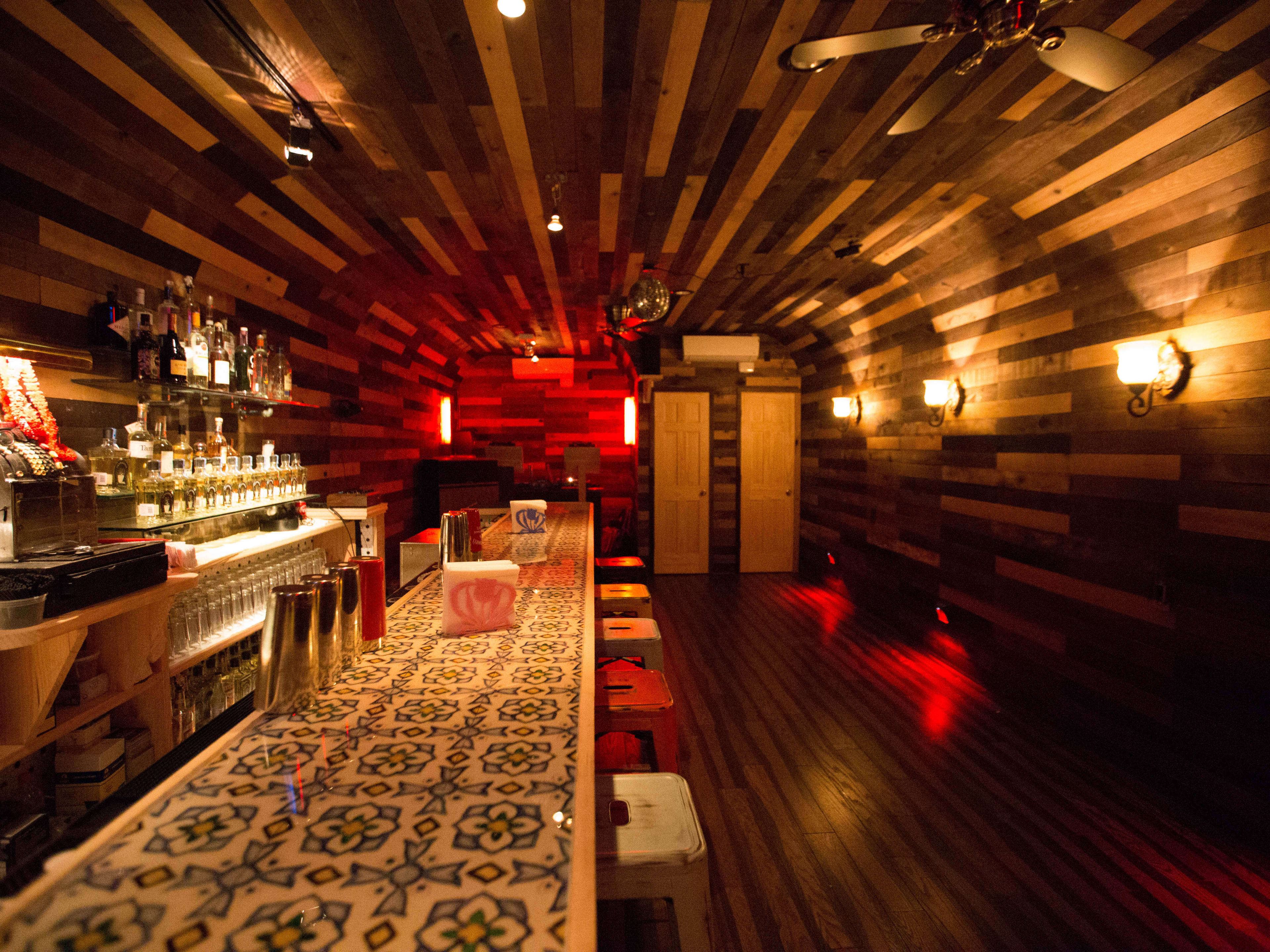 Mezcaleria La Milagrosa interiors with wood paneling on the walls and ceiling and a patterned tile bar with metal stools