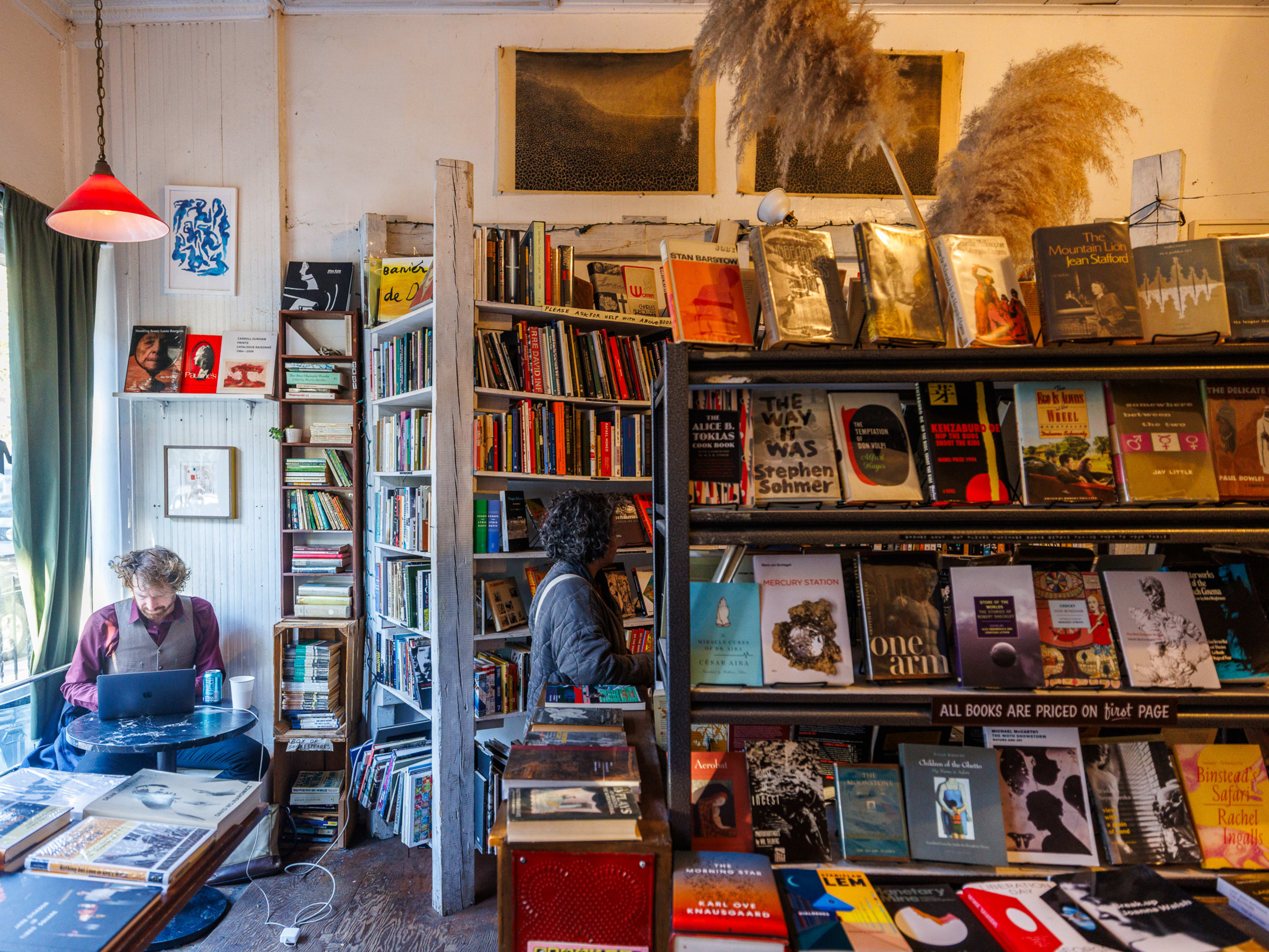 Molasses Books interior with a customer sitting at a small circular table in the window and books lining long bookshelves