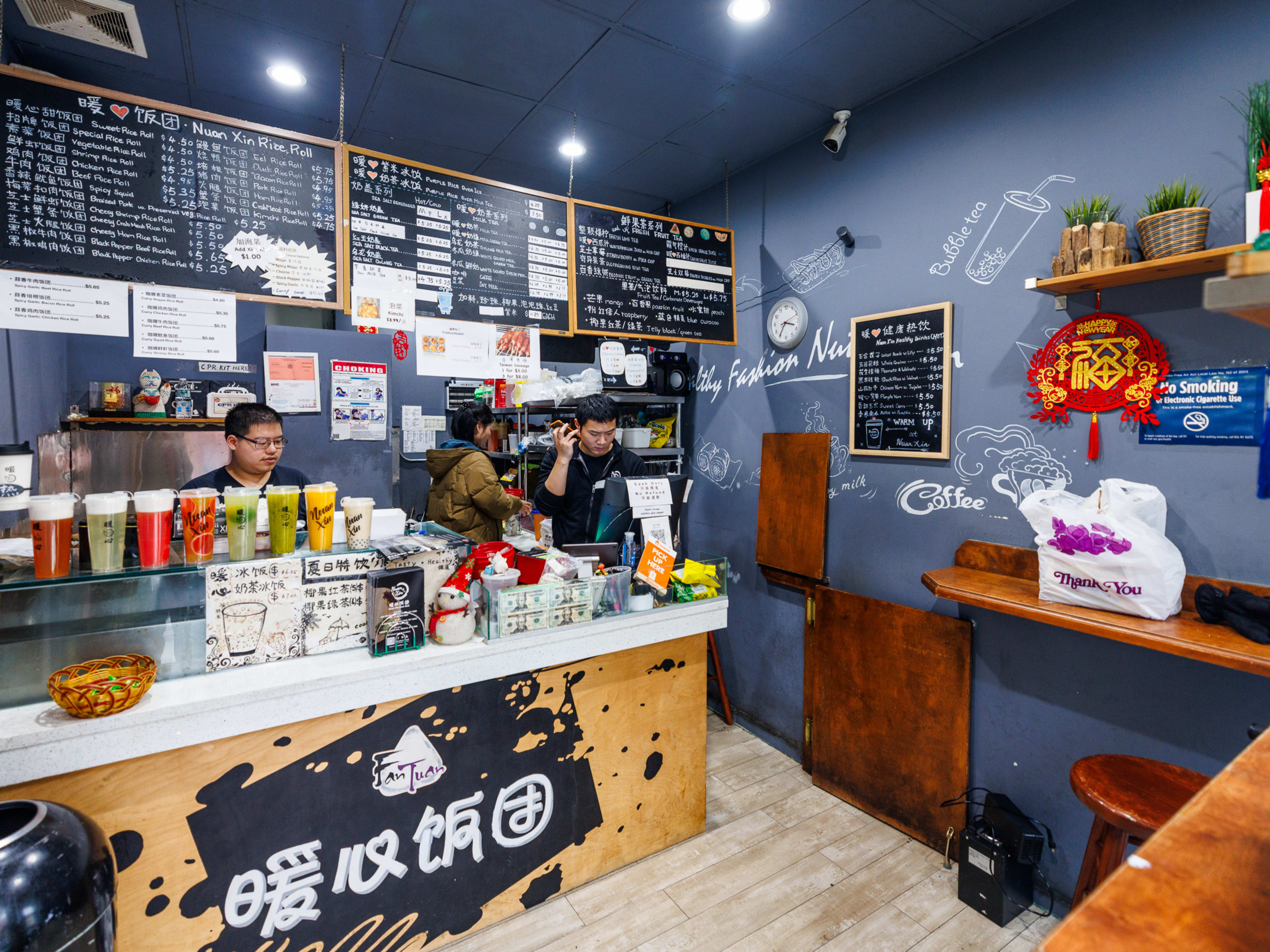 Nuan Xin Rice Roll interiors with a counter to order at on the left, chalkboard menus hanging above the counter, and a wooden counter with stools to sit at on the right