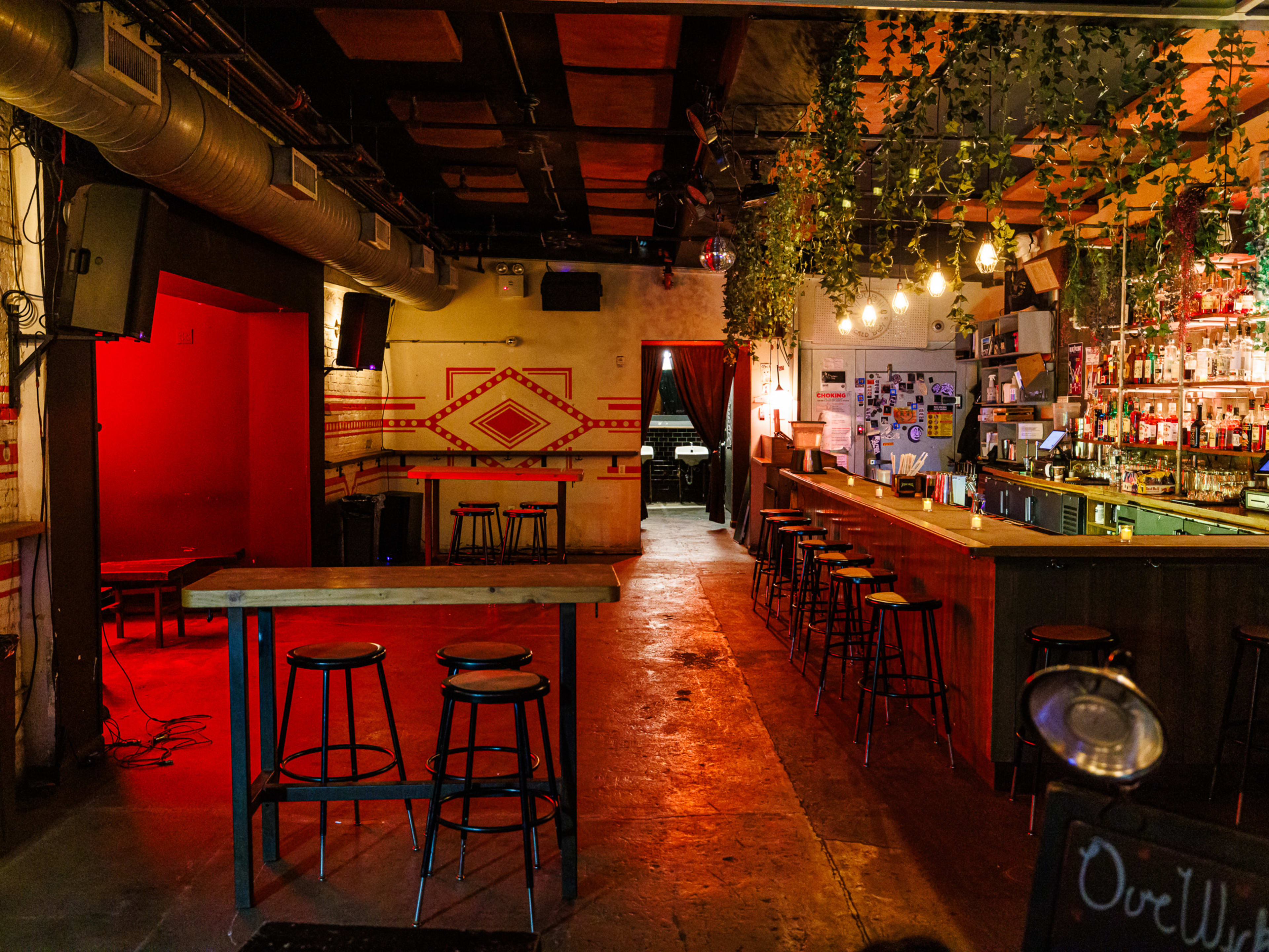 Our Wicked Lady interiors with vines hanging from the ceiling over the bar, dim red lighting, and high top counter seating.