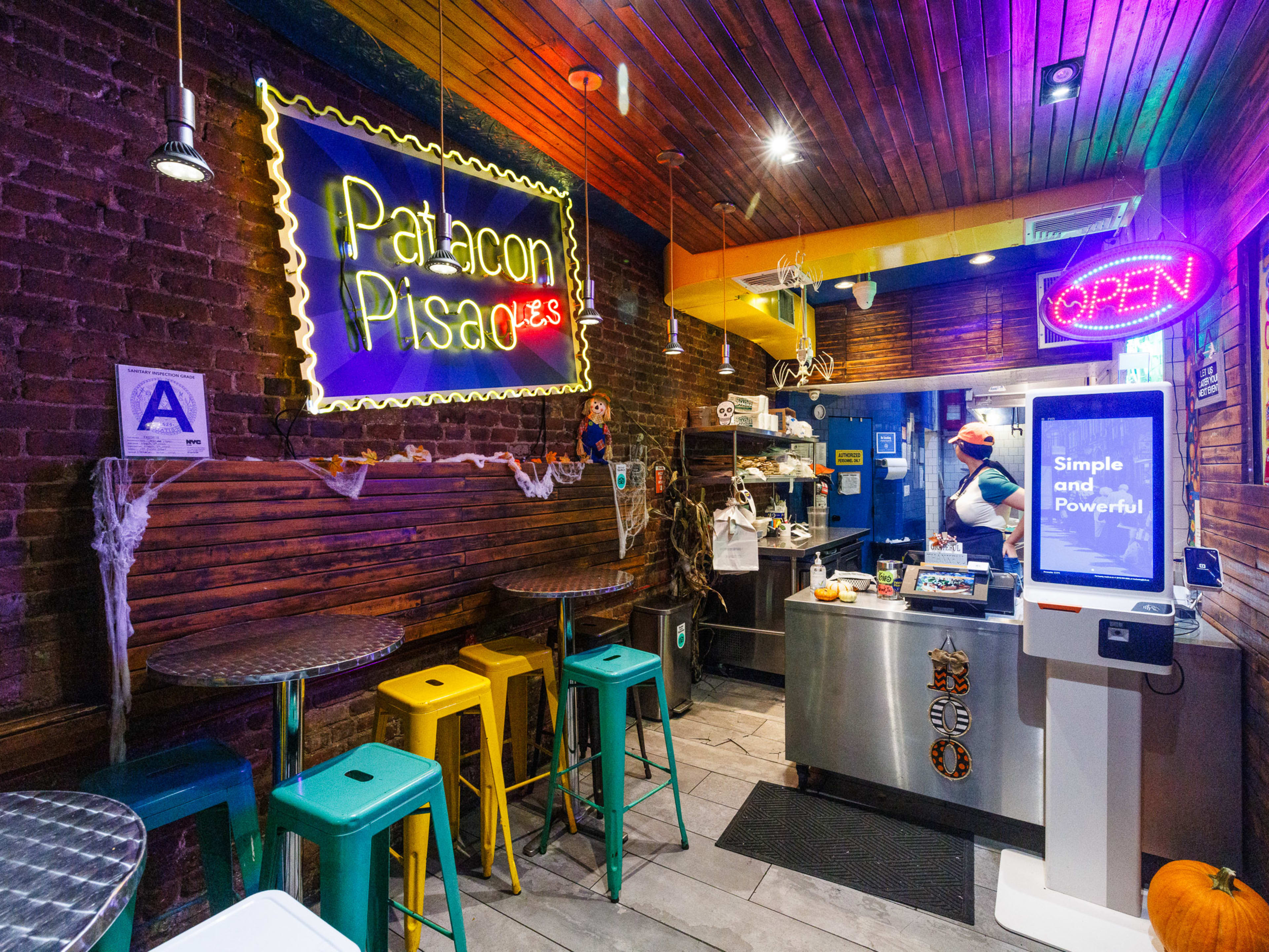 Patacon Pisao interiors with brick walls, multiple neon signs, silver high top tables, and a counter to order at