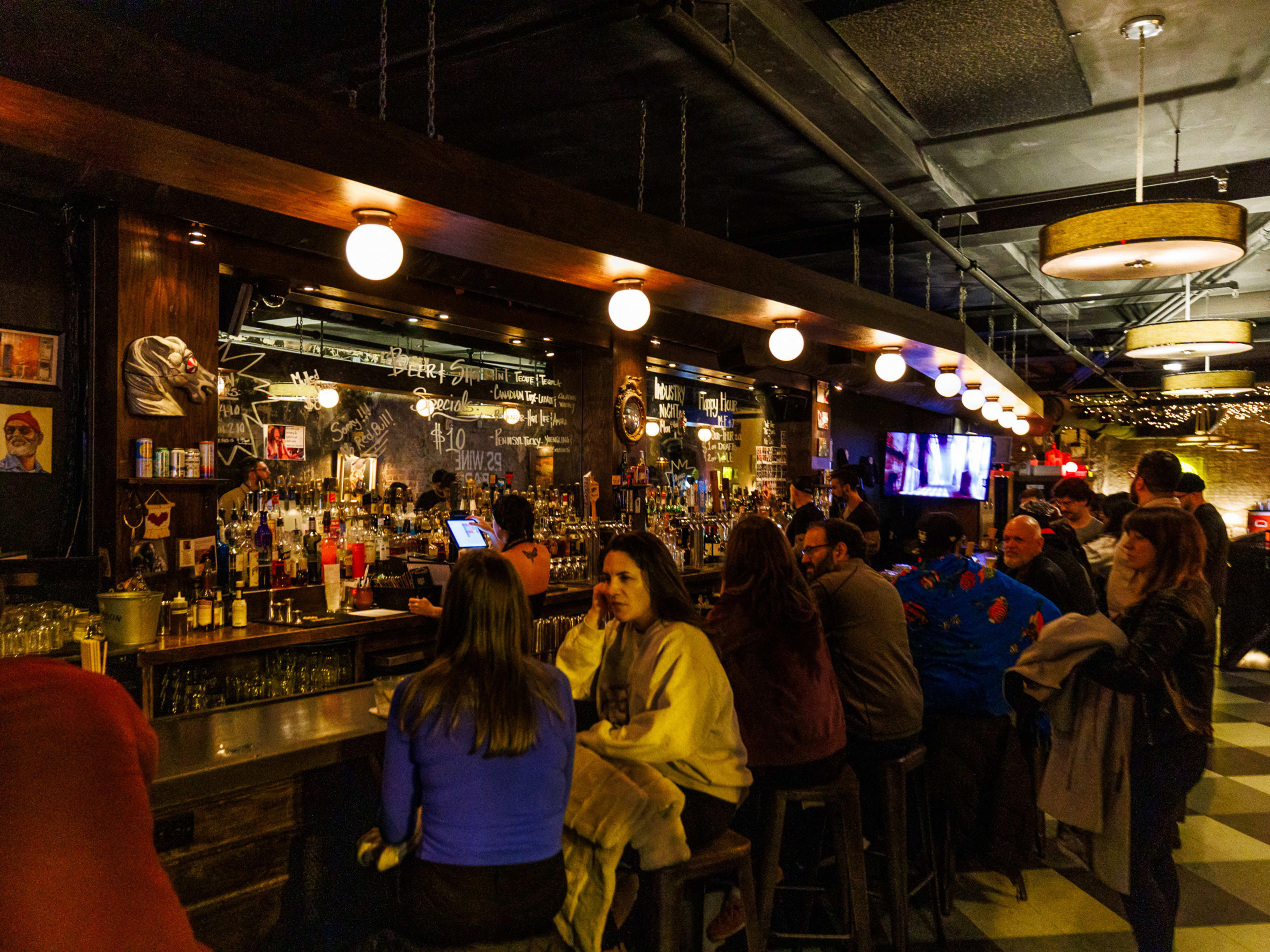 Pet Shop interiors with people seated at the bar, dim lighting, brick walls, and checkerboard floor tiles.