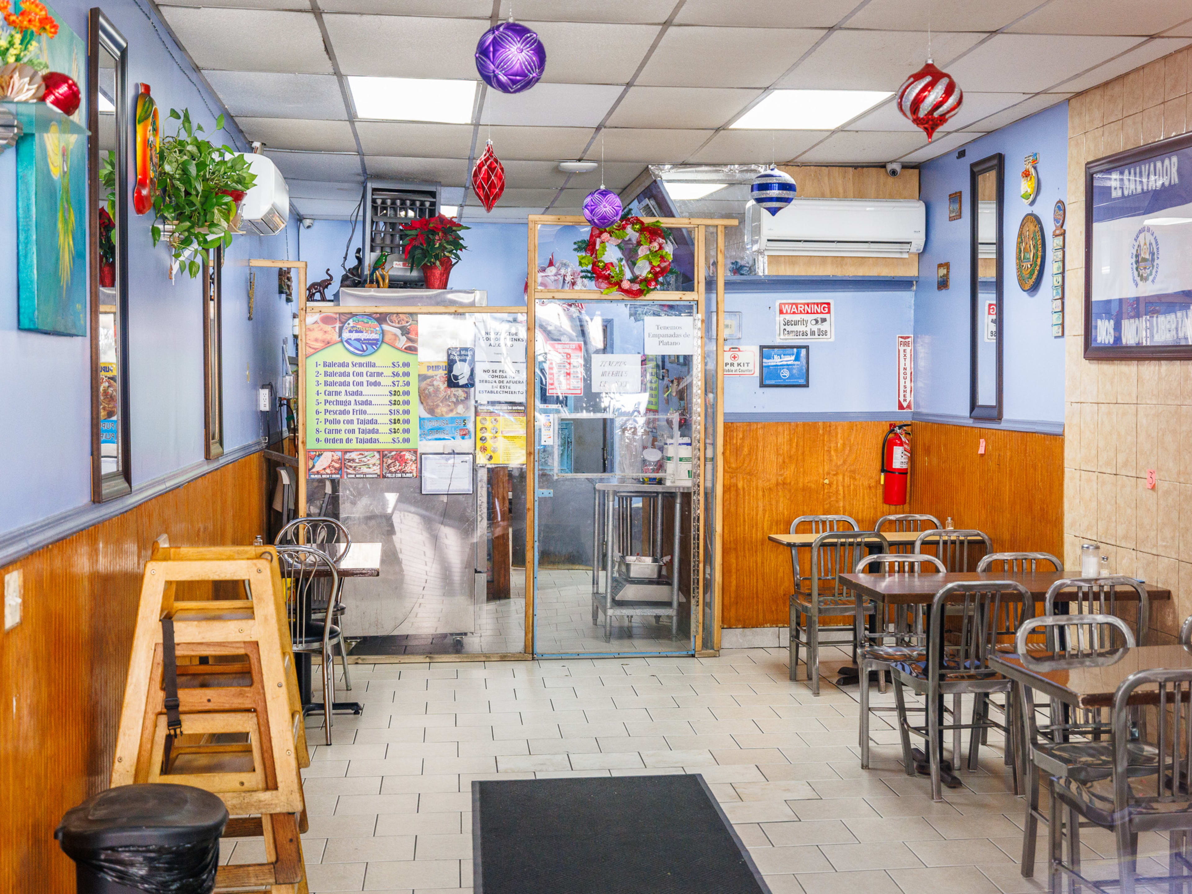 Pupuseria Salvadoreña interior with metal tables, blue walls, wood paneling, and ornaments hanging from the ceiling