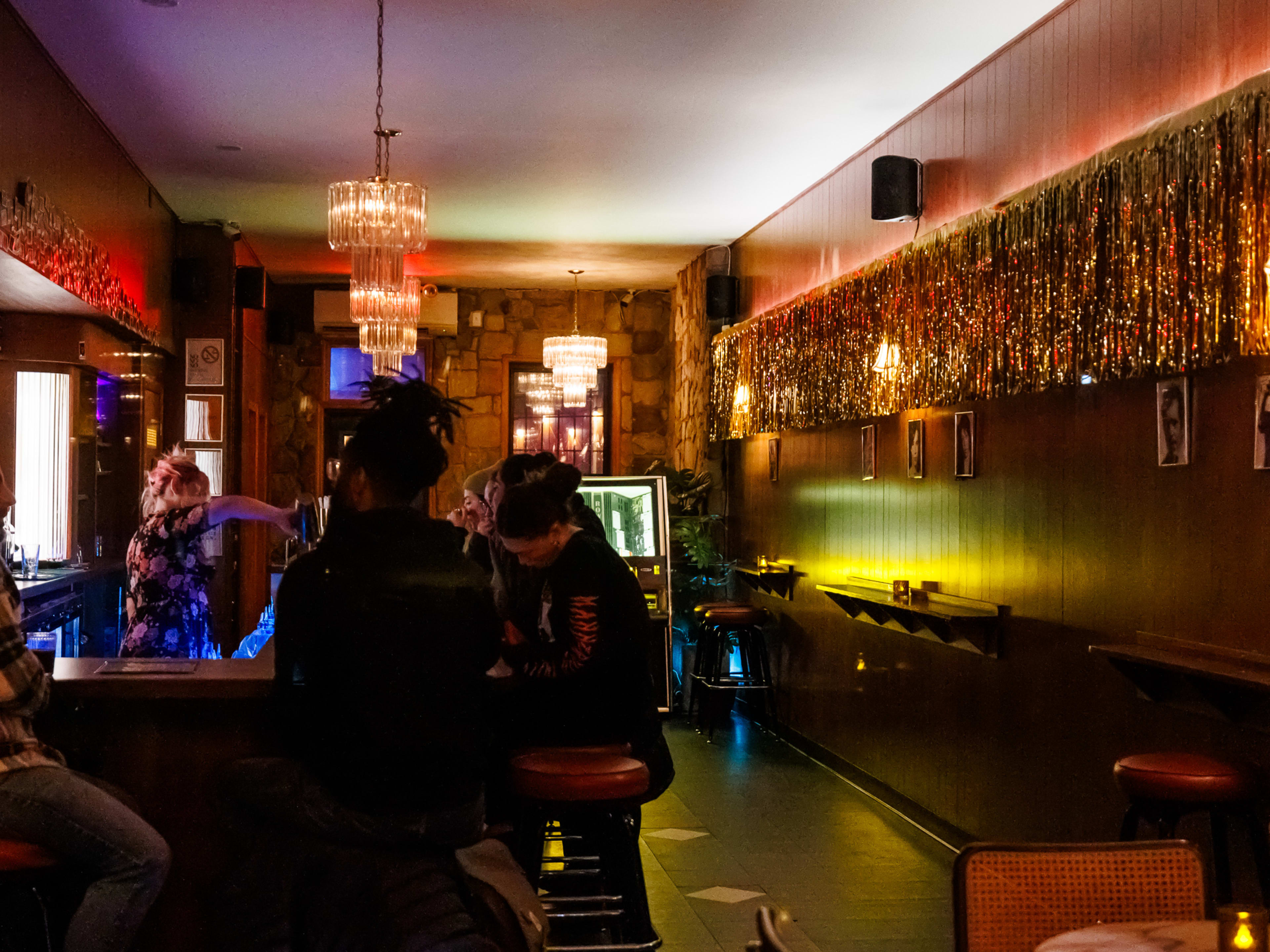 Rialto Grande interior with dim lighting, people seated at the bar on the left, wood paneled walls and gold streamers hanging