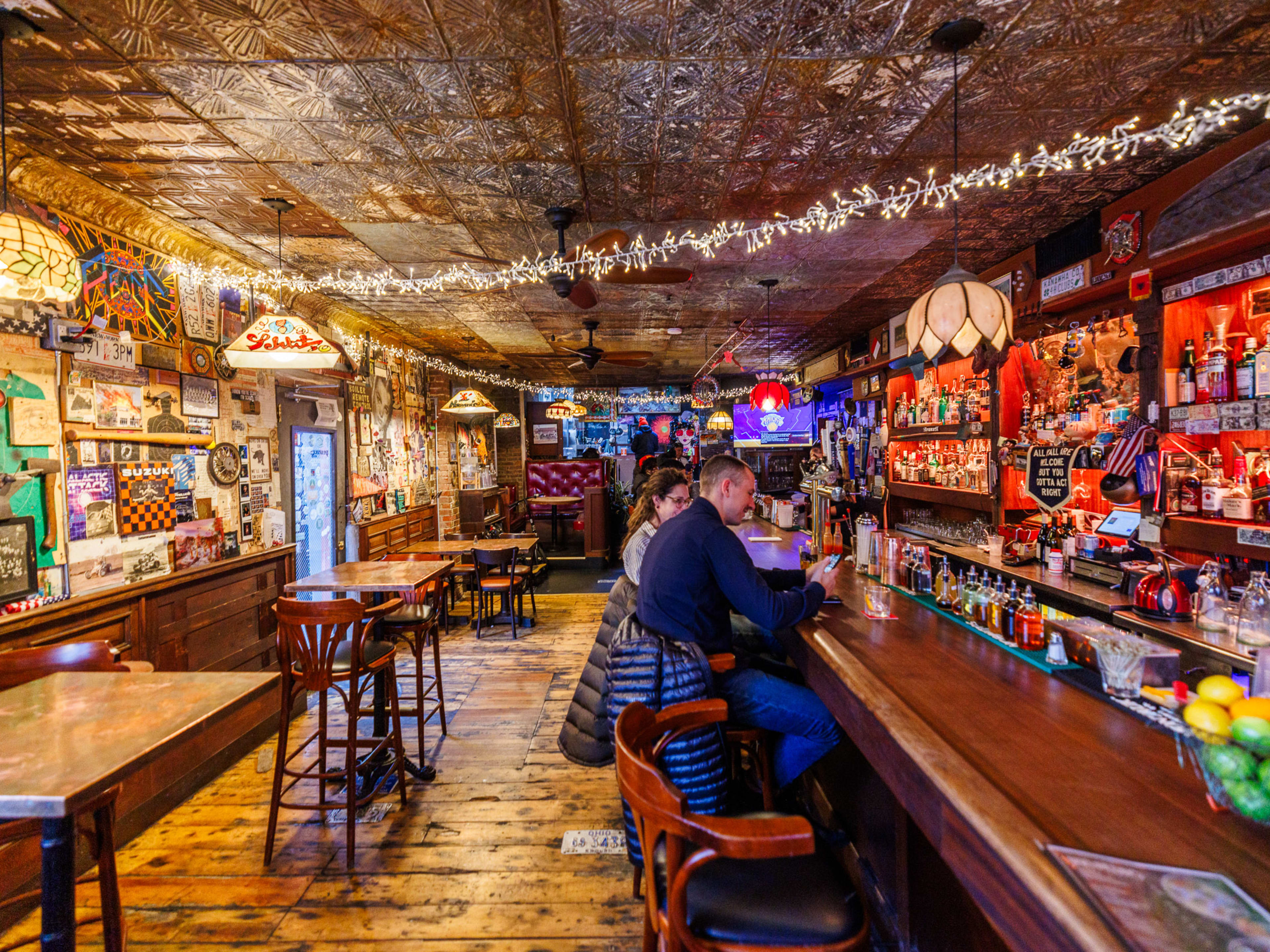 San Pedro interiors with string lights hanging across the ceiling, artwork filling the entire left wall, and customers seated at a long wooden bar on the right