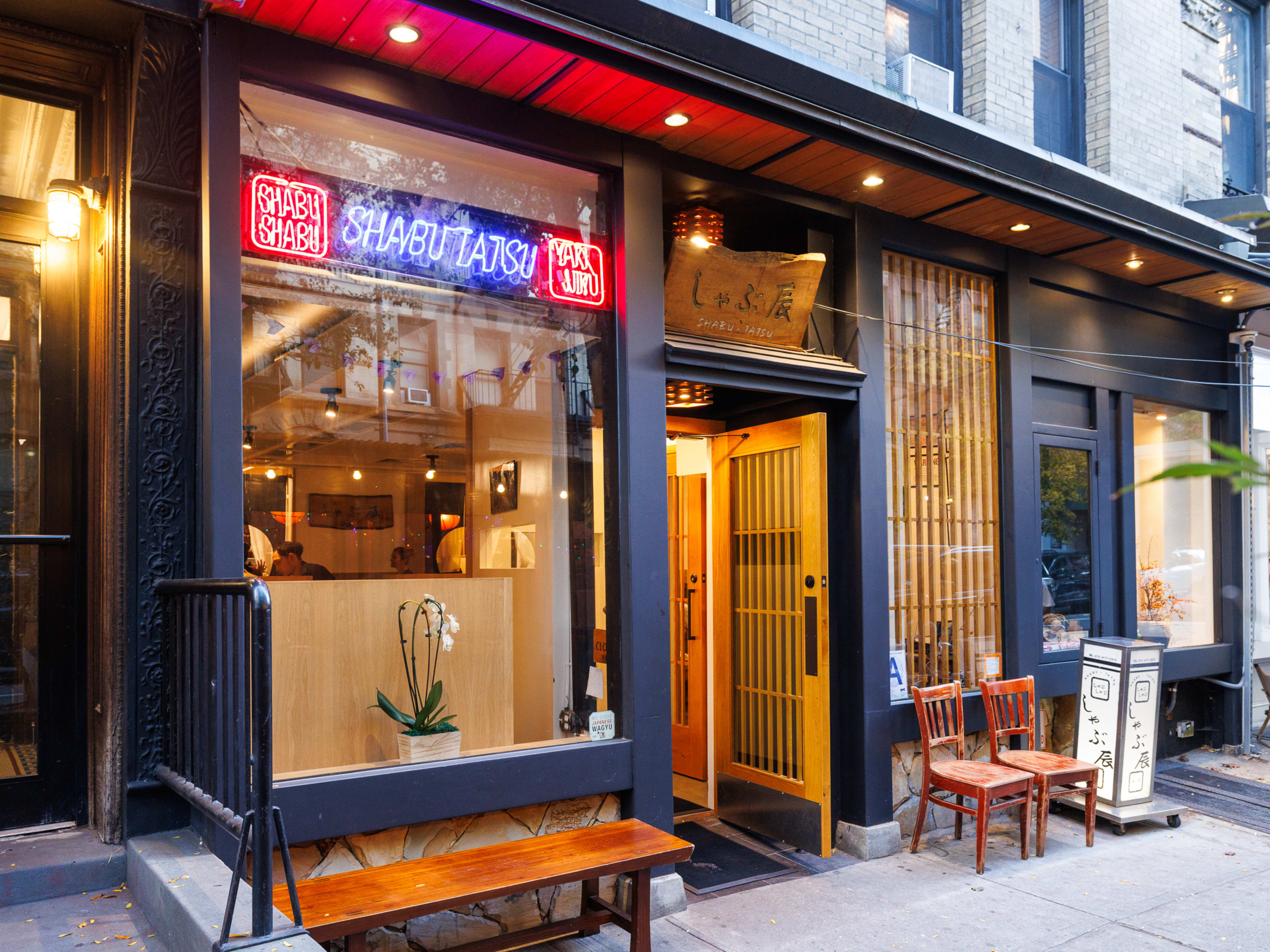 Shabu-Tatsu exterior with neon sign and wooden chairs and a bench out front