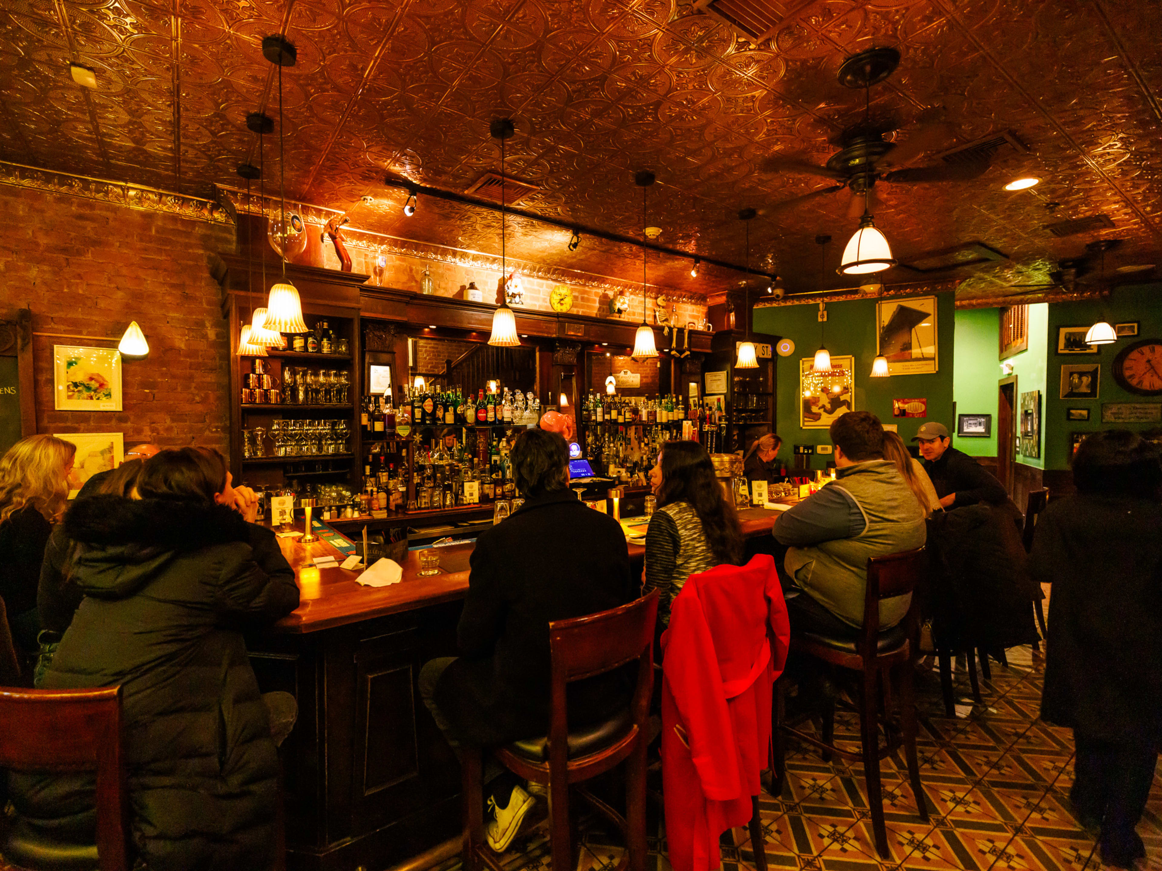 Skinner's Loft interiors with people seated at the bar, dim lighting, liquor bottles on shelves behind the bar, and a gold ceiling.