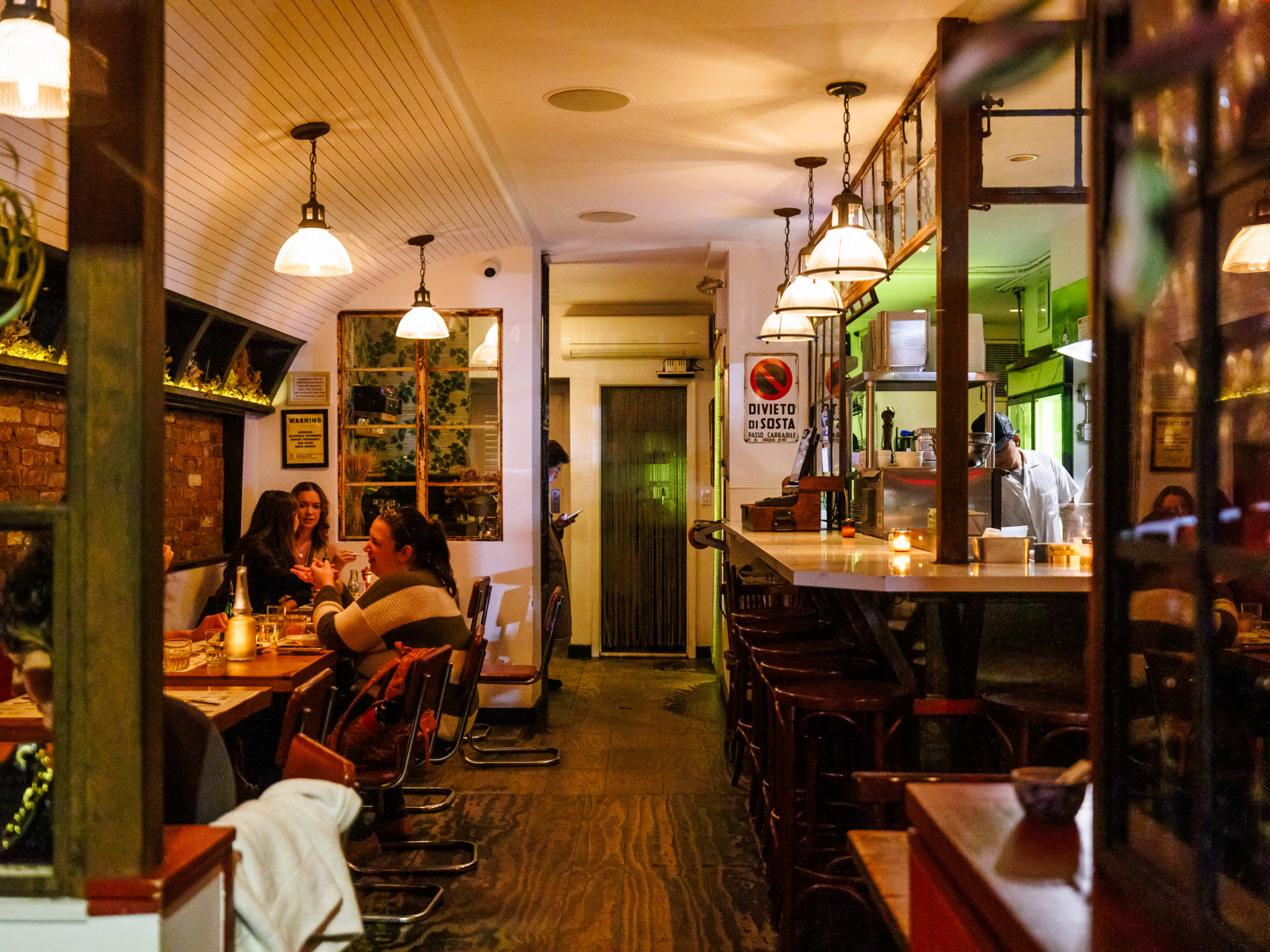 Spaghetti Incident interiors with dim lighting, candles on the bar to the right, and people seated at square wooden tables on the left