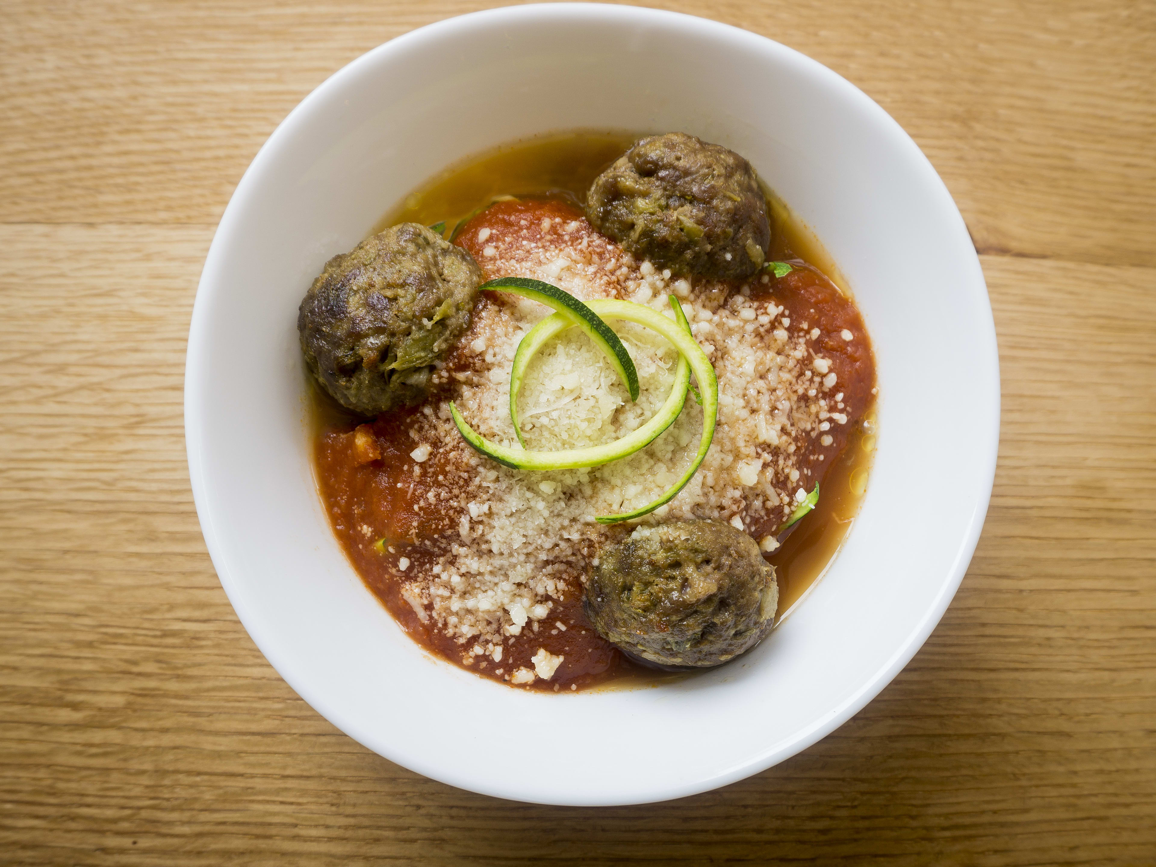 Bowl of meatballs with sauce and parmeasean cheese on a wooden table