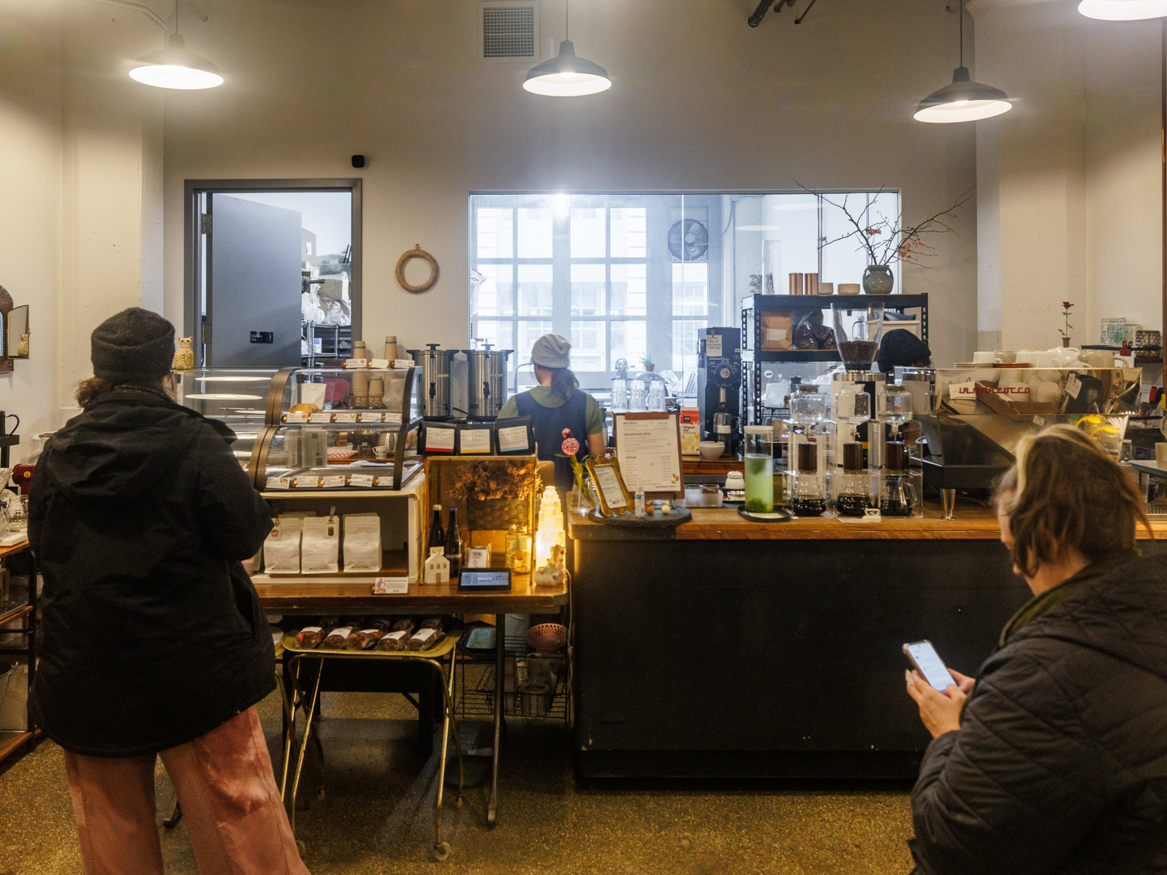 Tadaima interiors with customers waiting to order at the counter and pastries and bags of coffee beans on display on the shelves