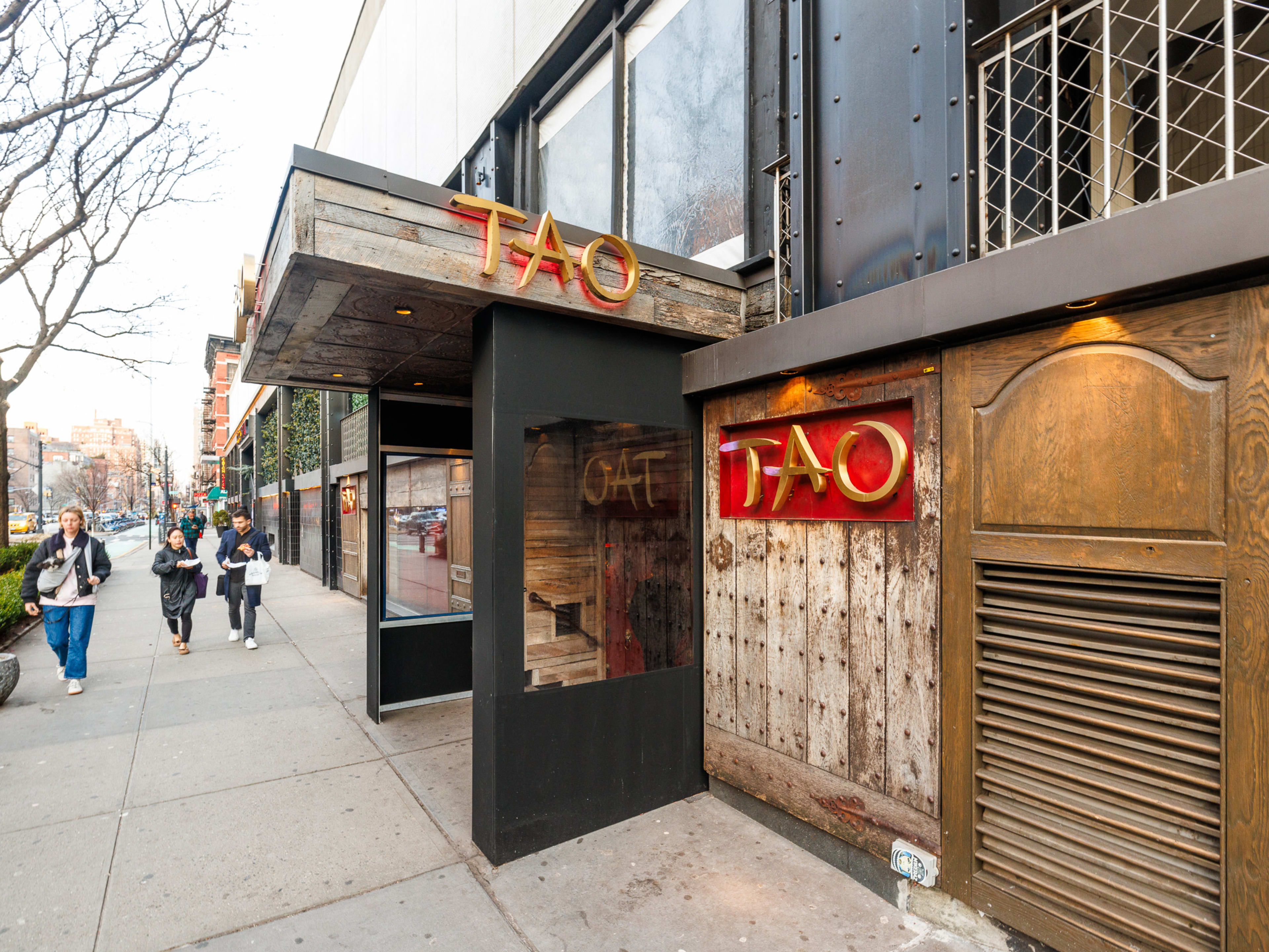 Tao Downtown exterior with large wooden restaurant sign and people walking by on the sidewalk out front