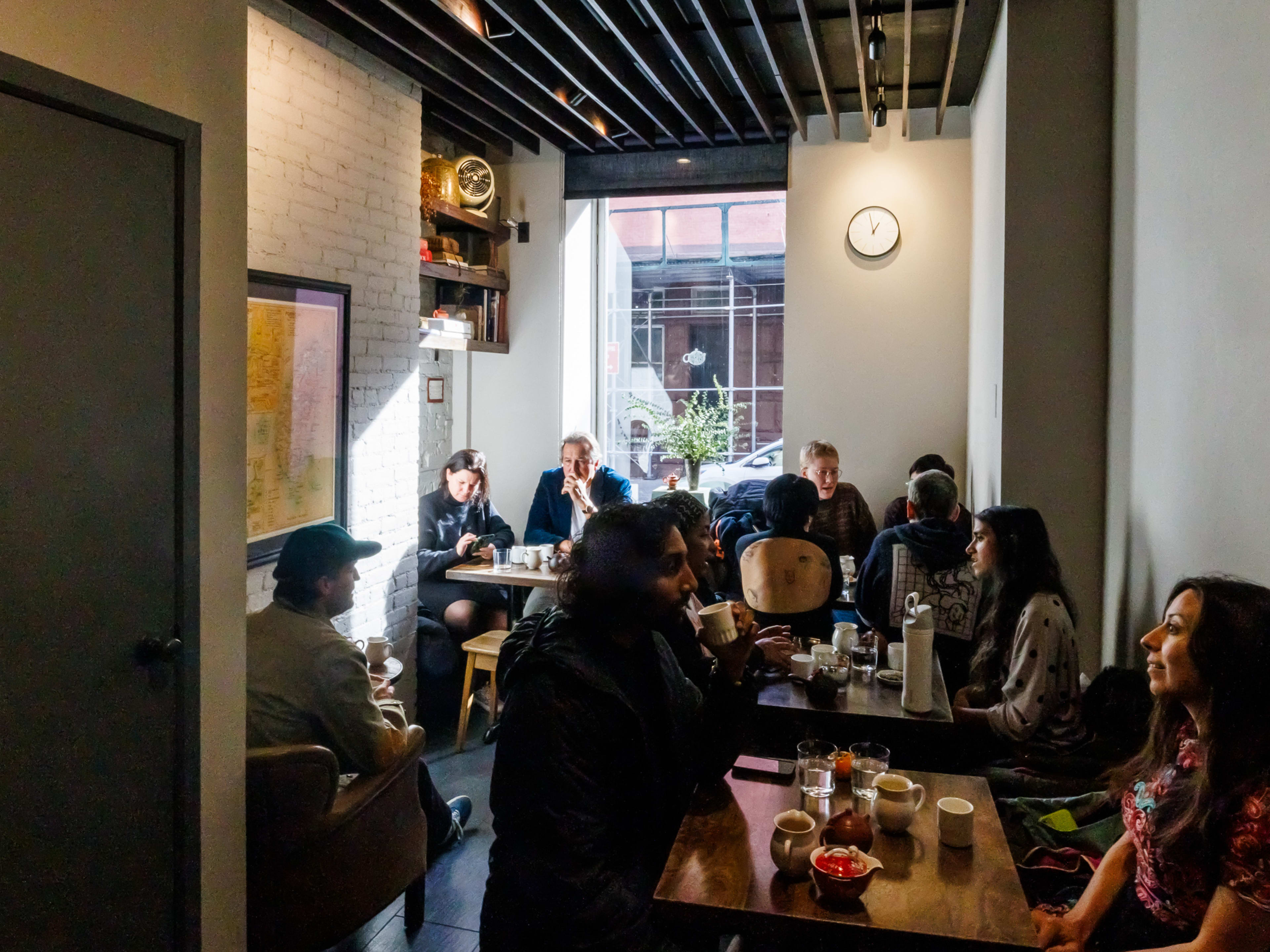 Té Company interiors with white brick walls, a large window looking out onto the street, and people seated at square wooden tables