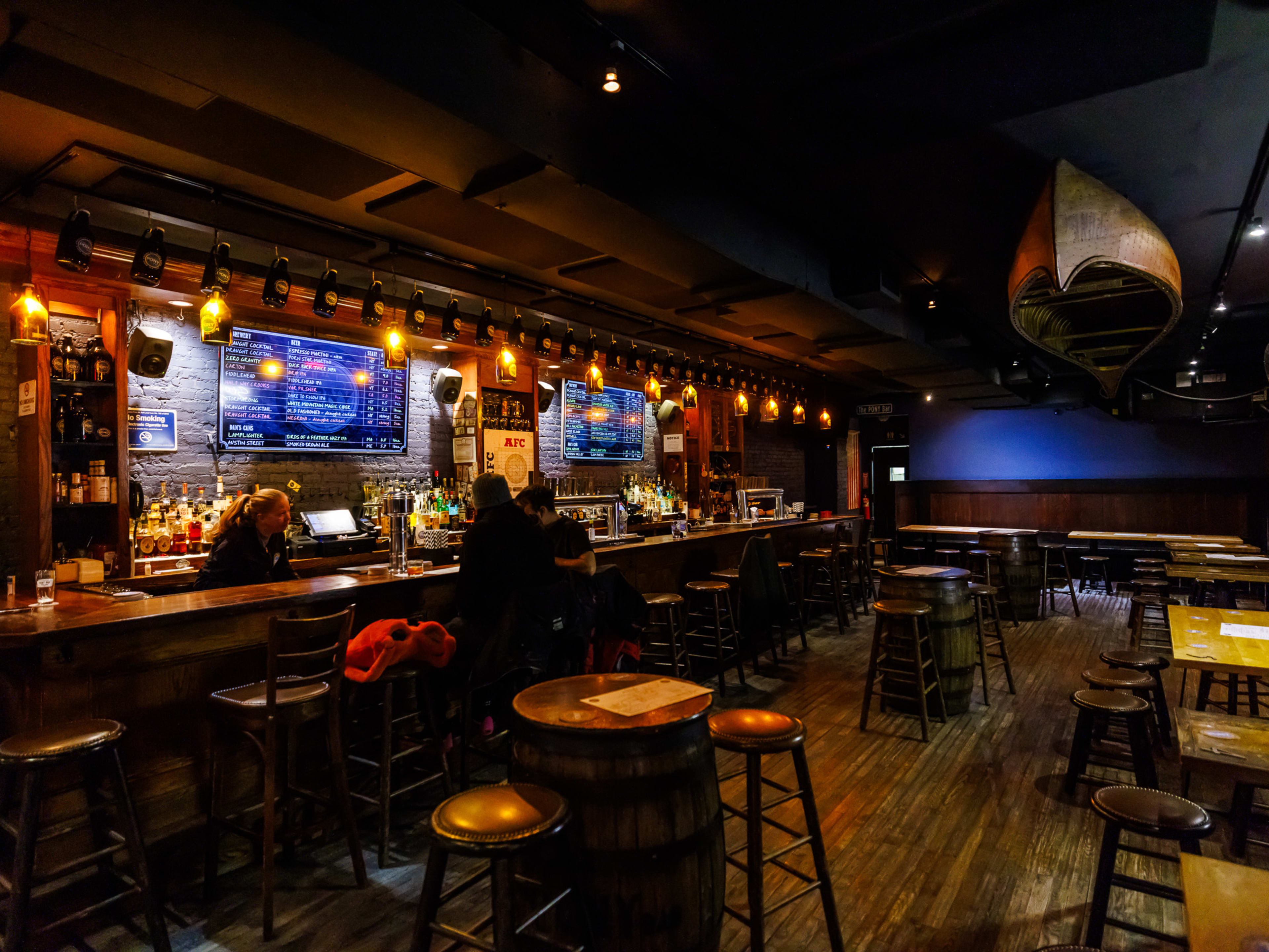 The Pony Bar interiors at night with two people seated at the bar on the left and multiple empty wooden tables and stools on the right