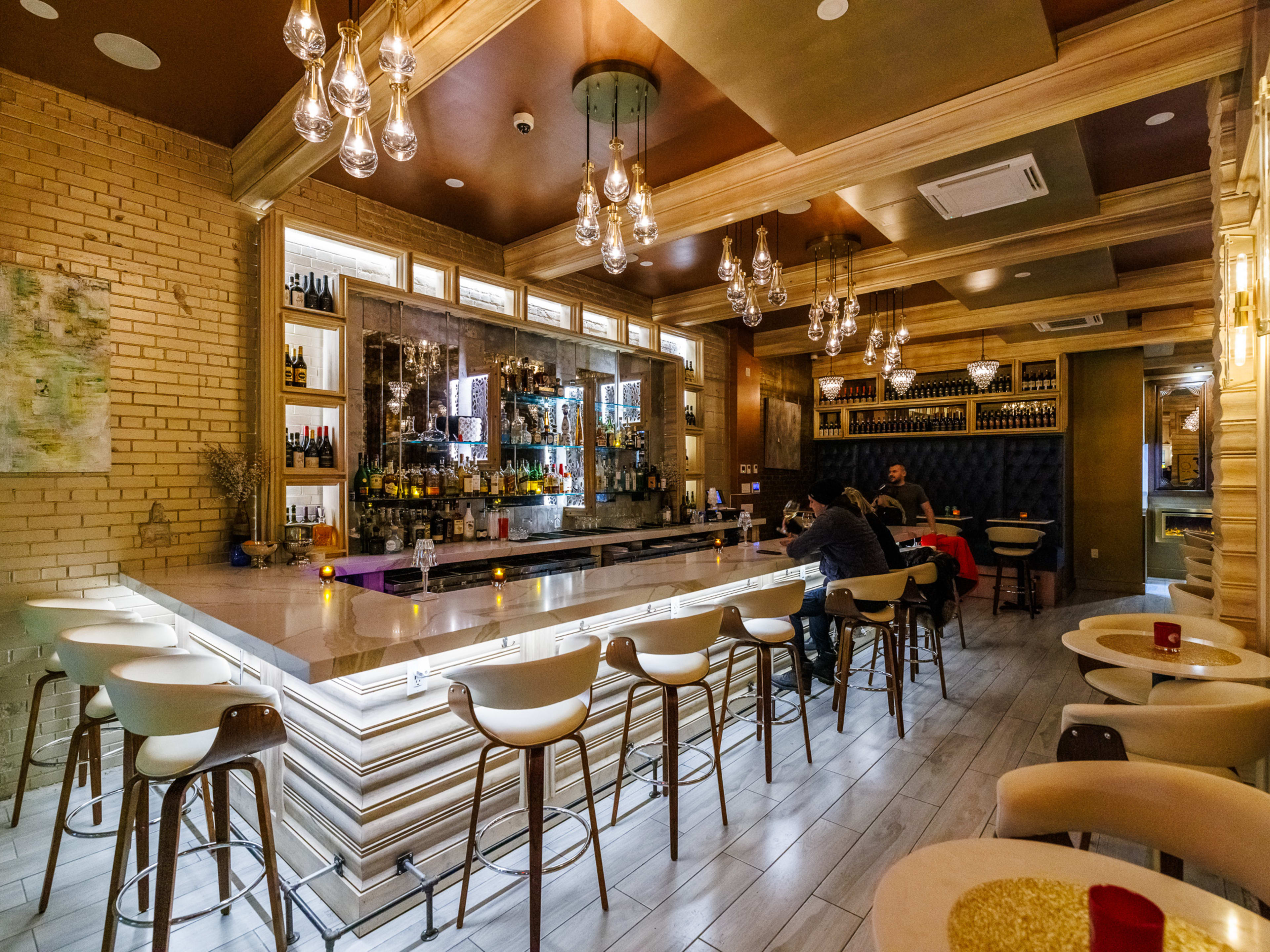 Vero interiors with a light up bar, multiple hanging light fixtures, white brick walls, and small circular tables with cushioned chairs