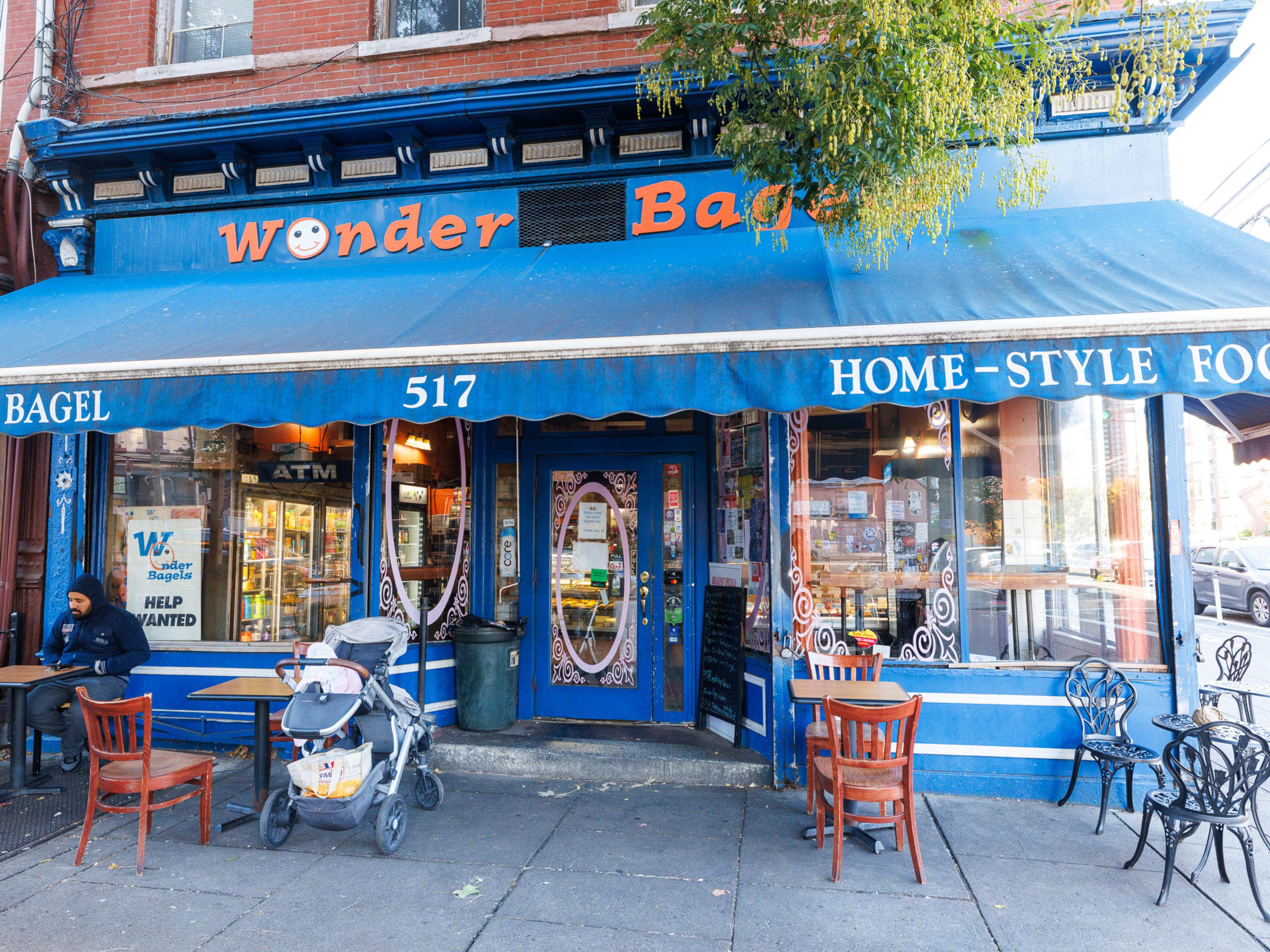 Wonder Bagels exterior with tables scattered on the sidewalk, blue walls, and a large awning