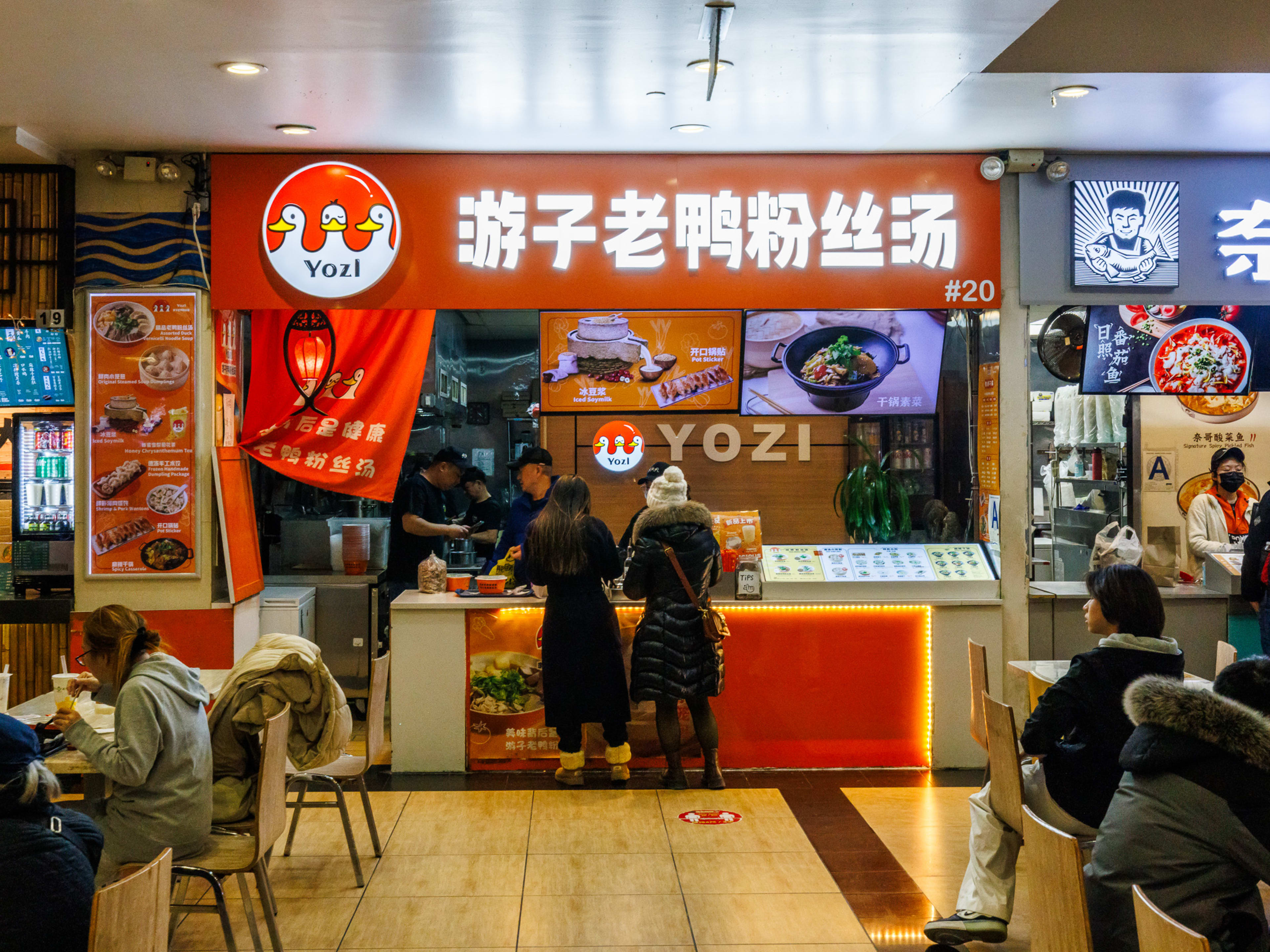 YOZ Shanghai Restaurant interiors with people ordering at the counter and people eating at square tables in front of the Yozi food stand