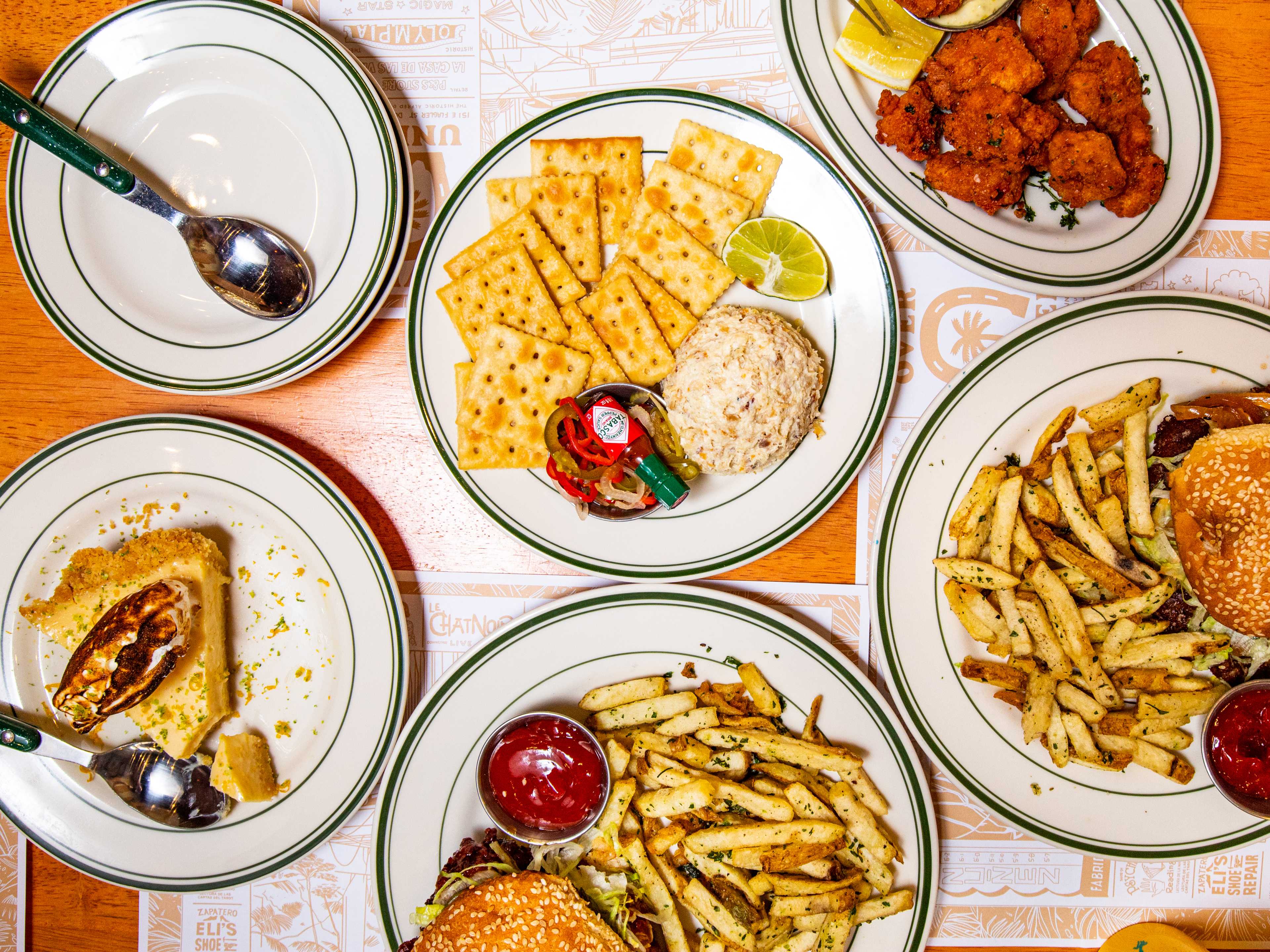 A cheeseburger, fish dip, and more plates shot from overhead on a wooden table.