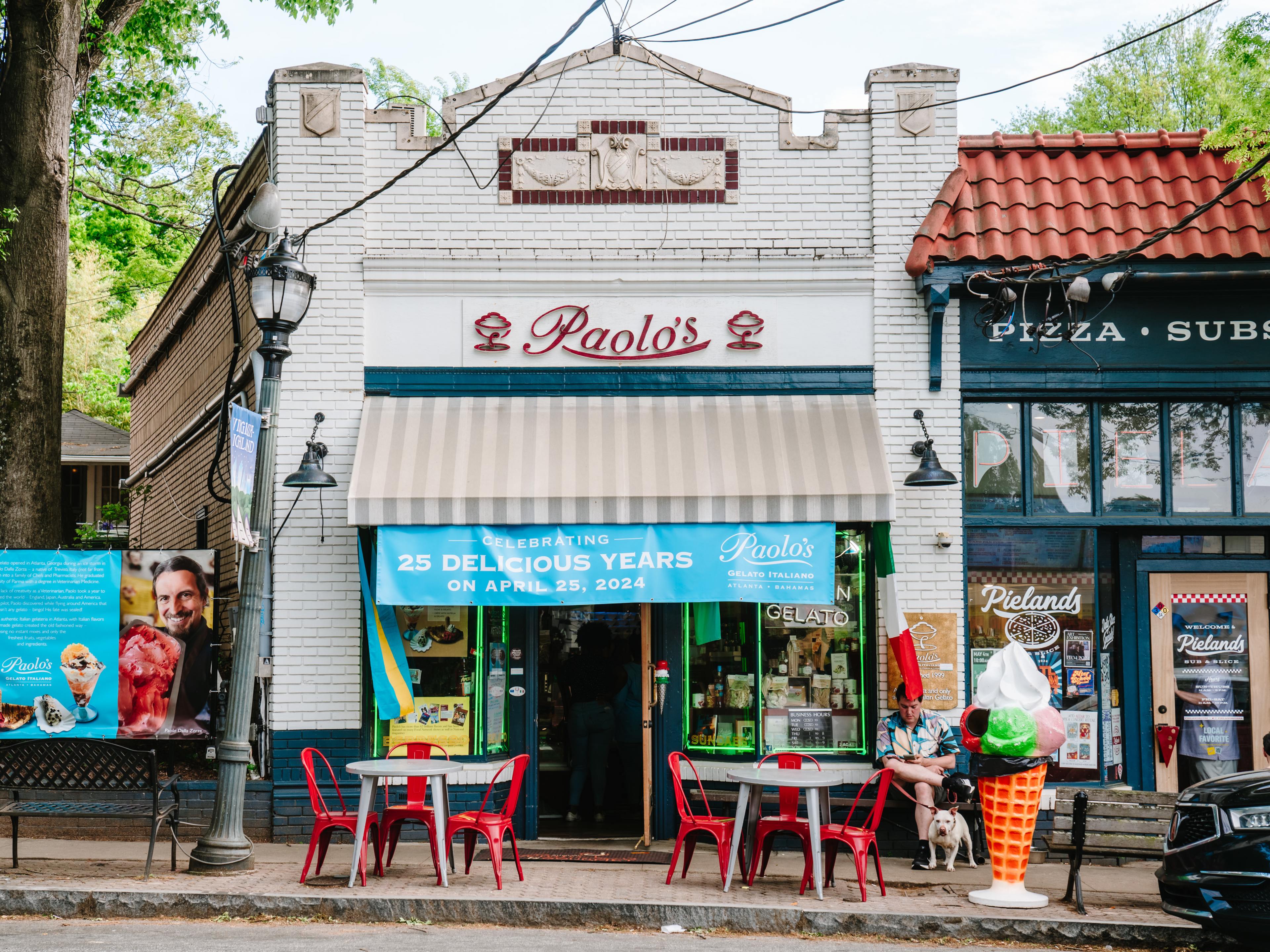 Exterior of white building with red logo featuring Paolo's name, with red bistro tables and a huge ice cream cone statue int front of the building.