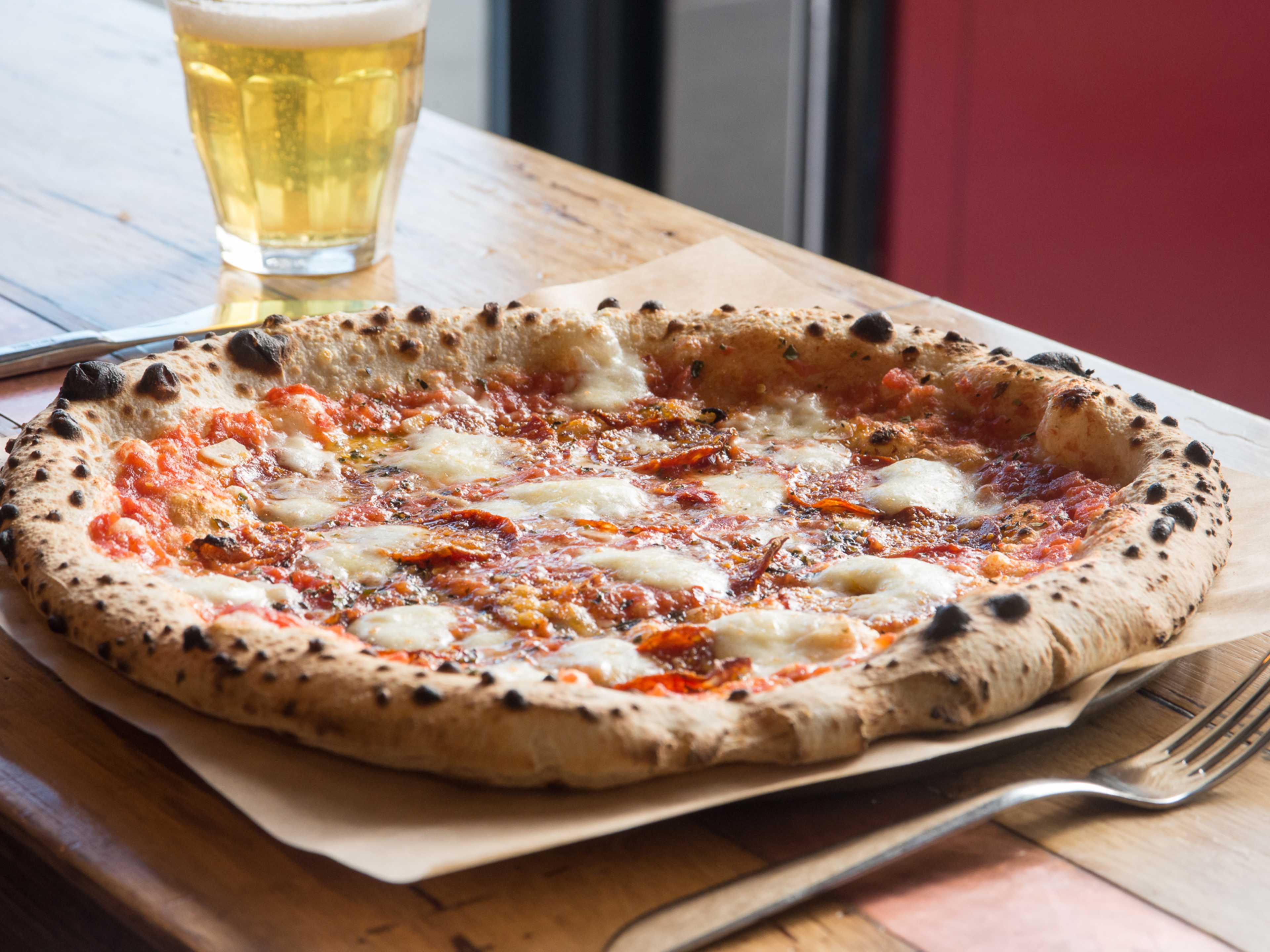 A pizza and a beer on a wooden table.