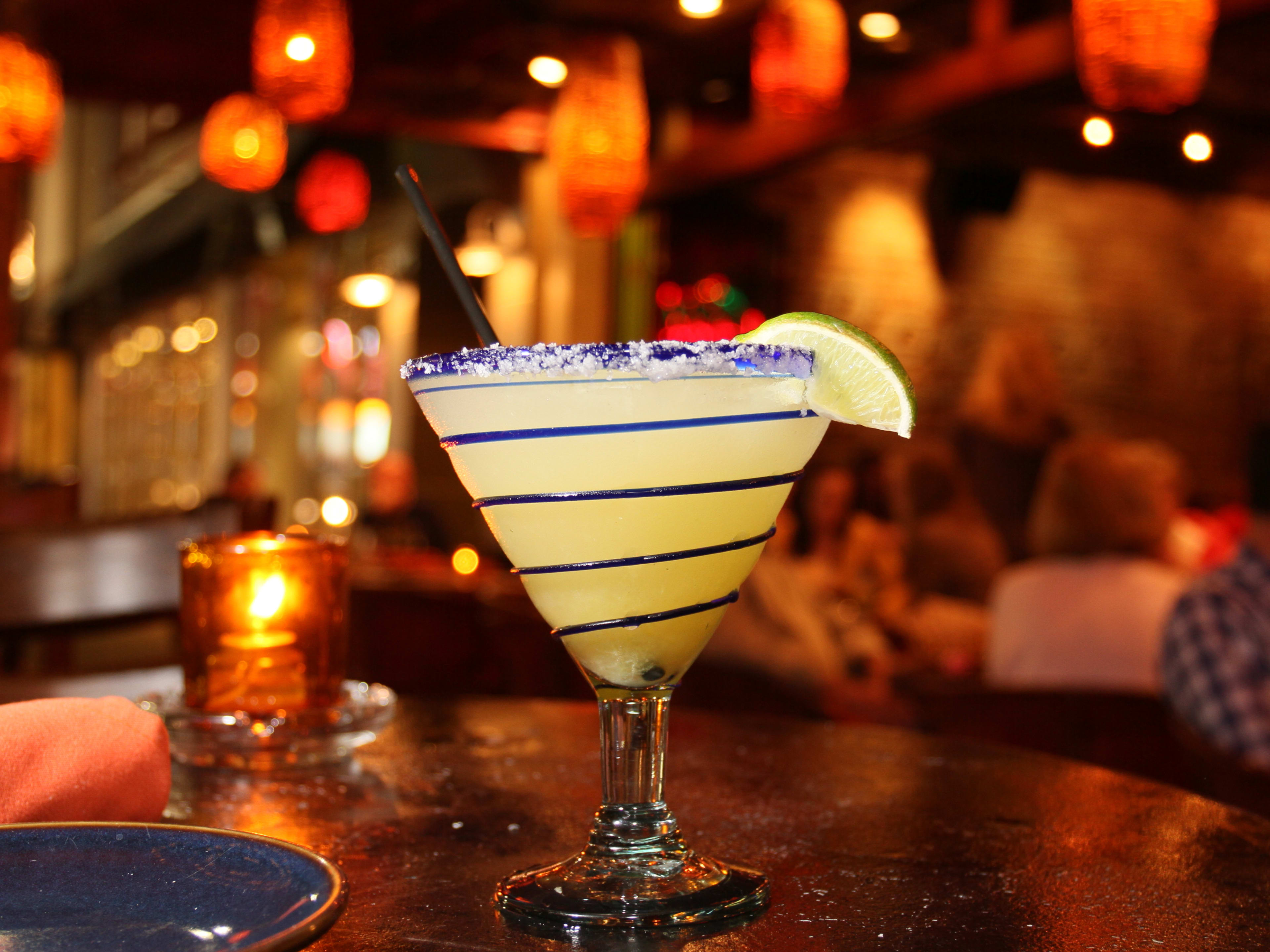 Margarita on a table with a candle and hanging lanterns in the background from Rocco's Tacos and Tequila Bar