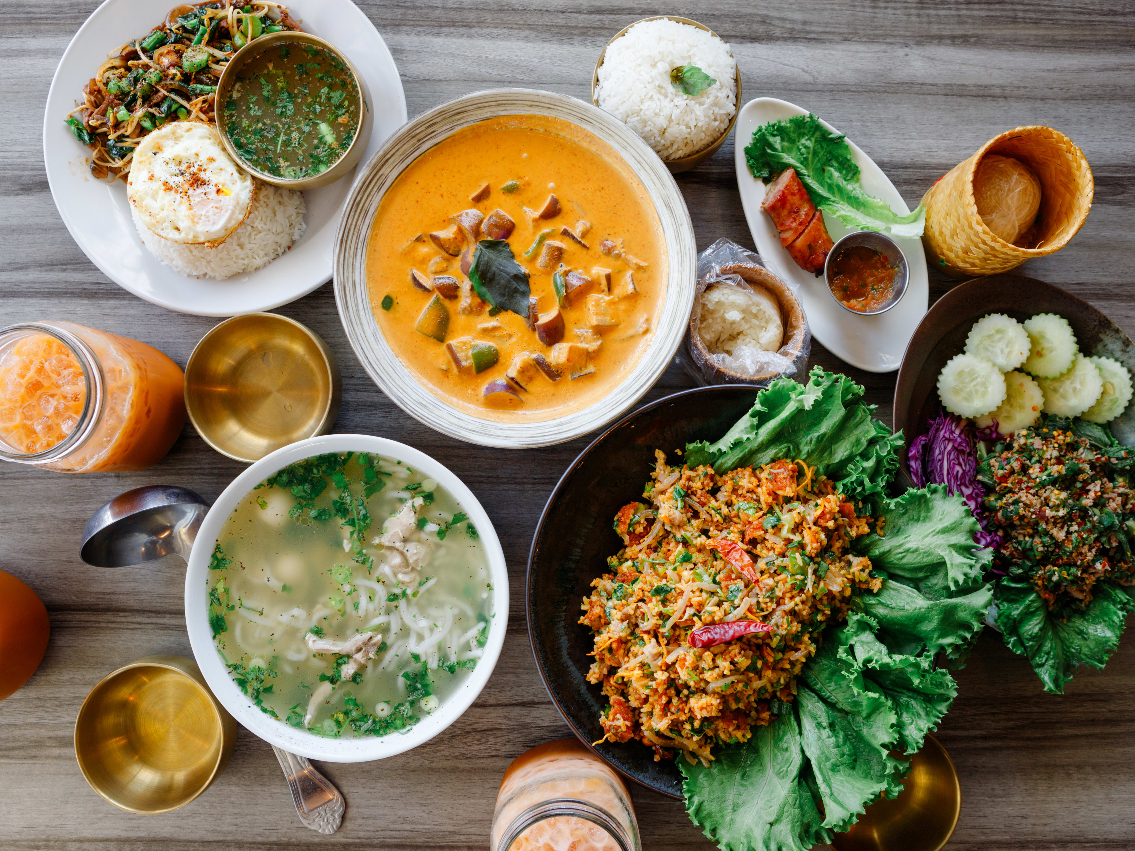 multiple plates of colorful thai food, rice, curry, and soup on a table