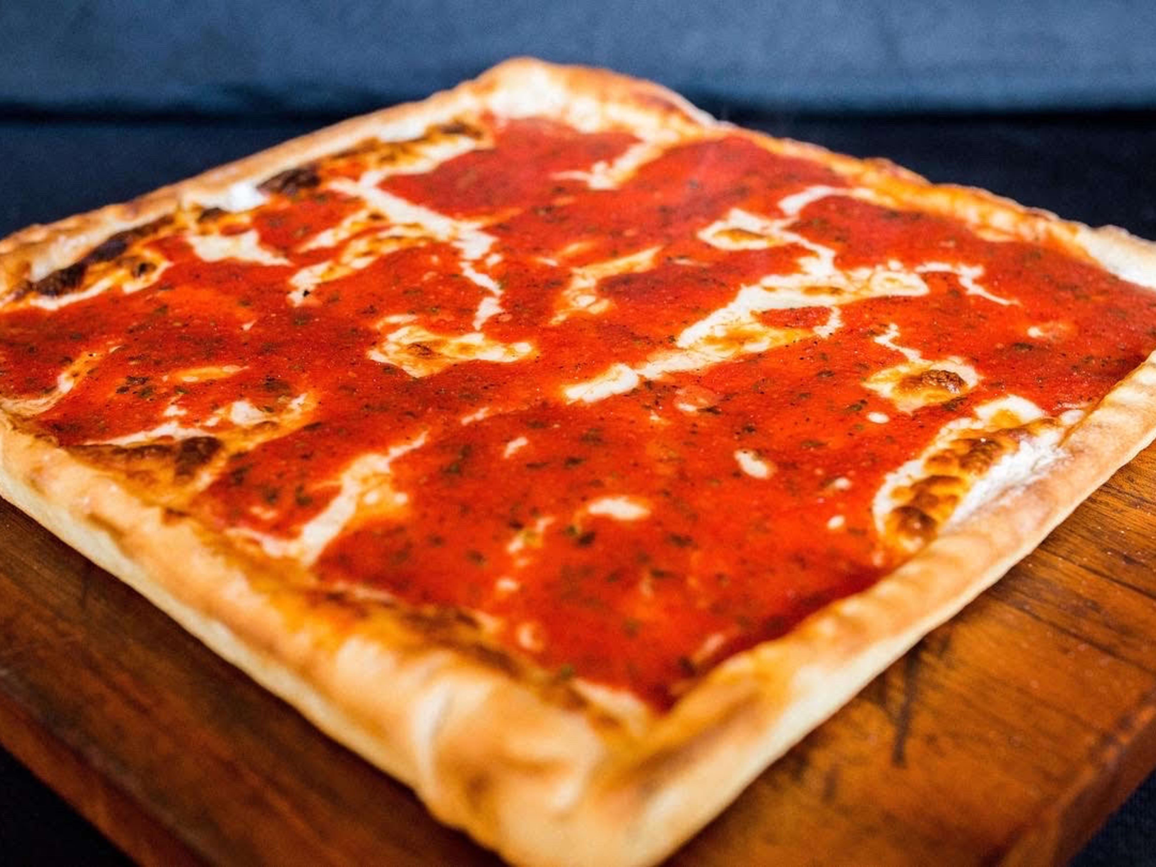 Santucci's Original Square Pizza on a wooden cutting board with tomato sauce and thick crust