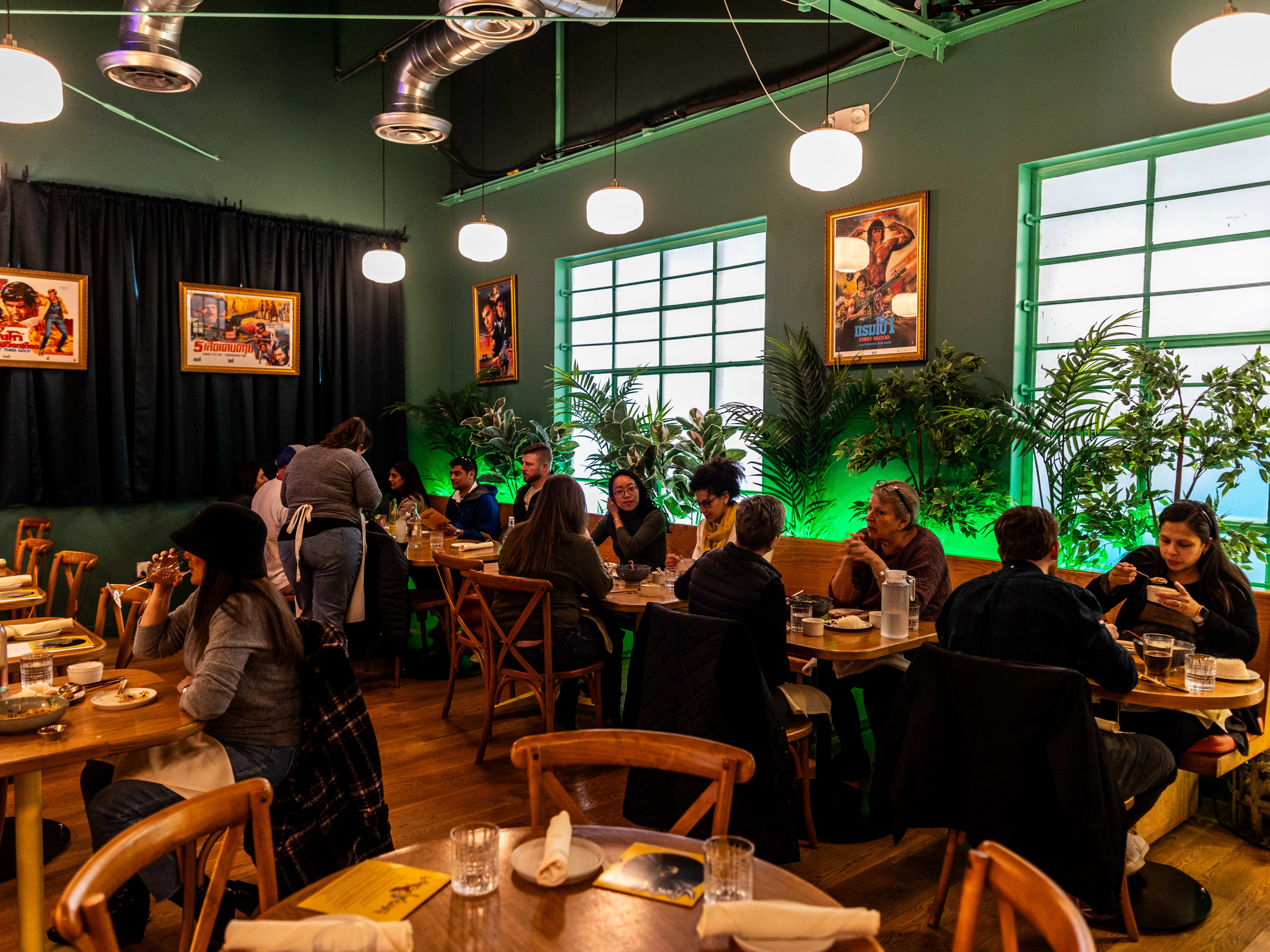 Street To Kitchen dining room with green walls, large metal-framed windows, and glowing green LED lights under a wall of tropical plants