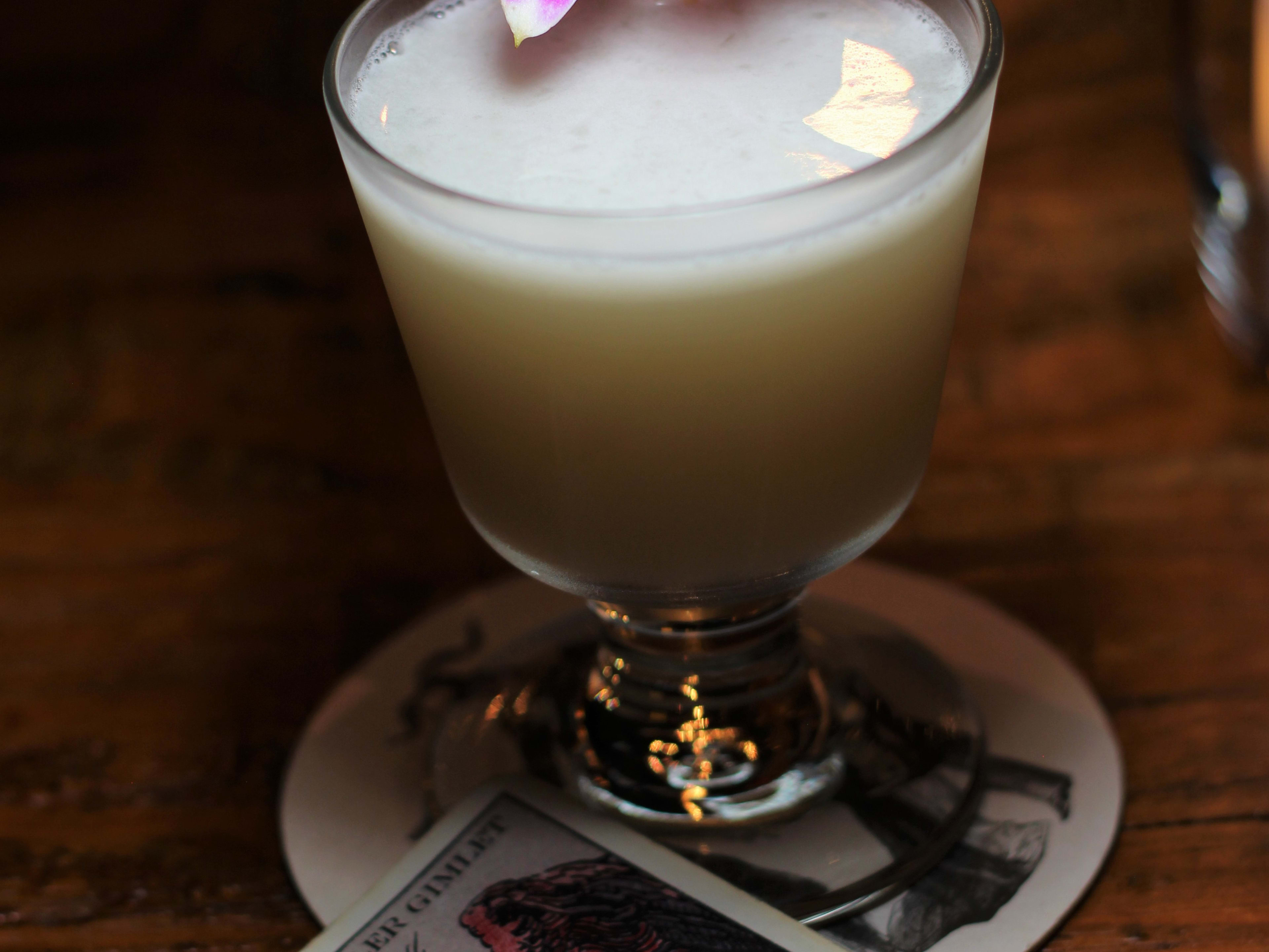 Close image of white cocktail with flower on top next to tarot card.