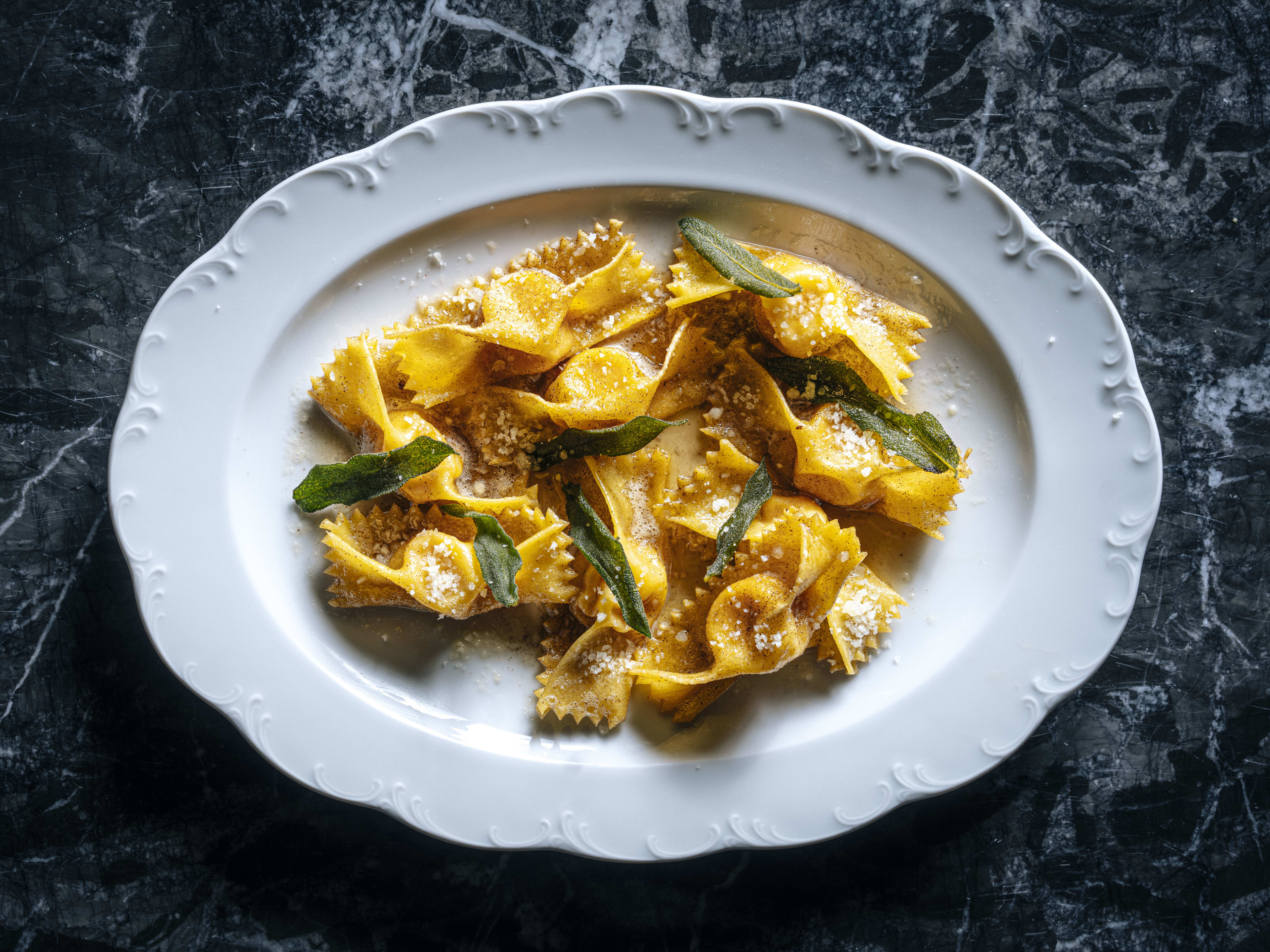 Tortelli topped with sage leaves on a scalloped white plate against a black marble background