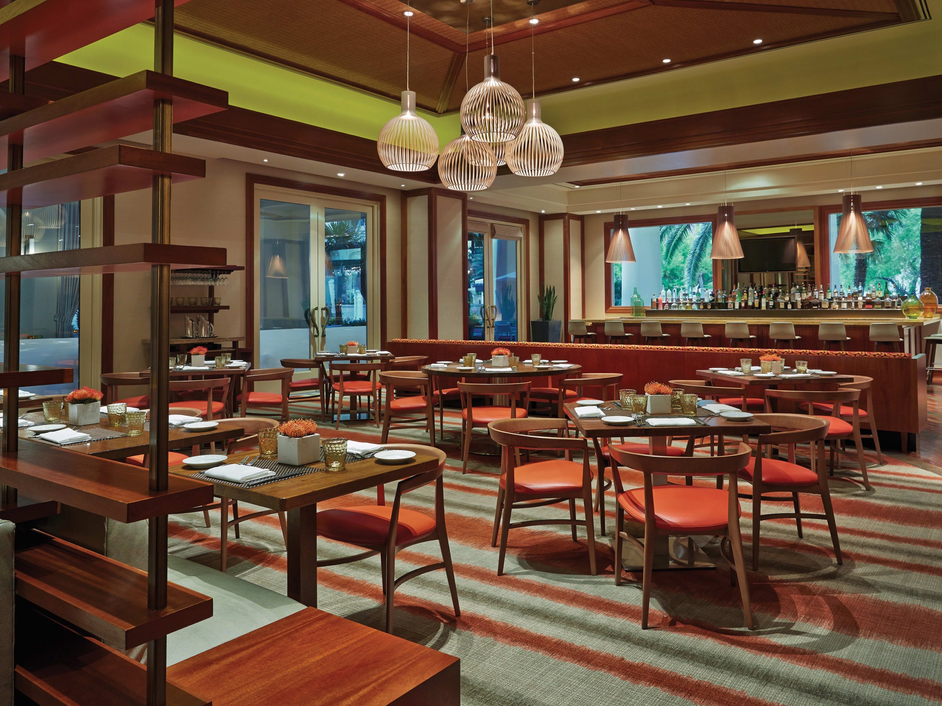 Veranda interiors with striped carpeted floors, square wooden tables, and a light fixture hanging in the center of the restaurant