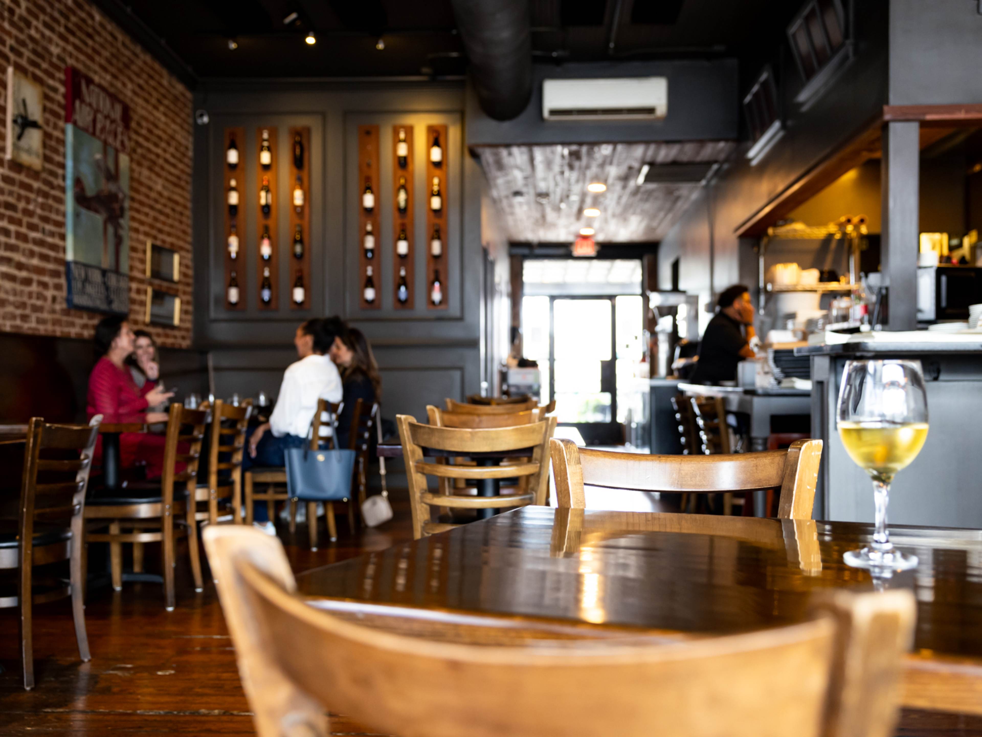 Inside of restaurant with brick walls and wooden chairs and wine display in background.