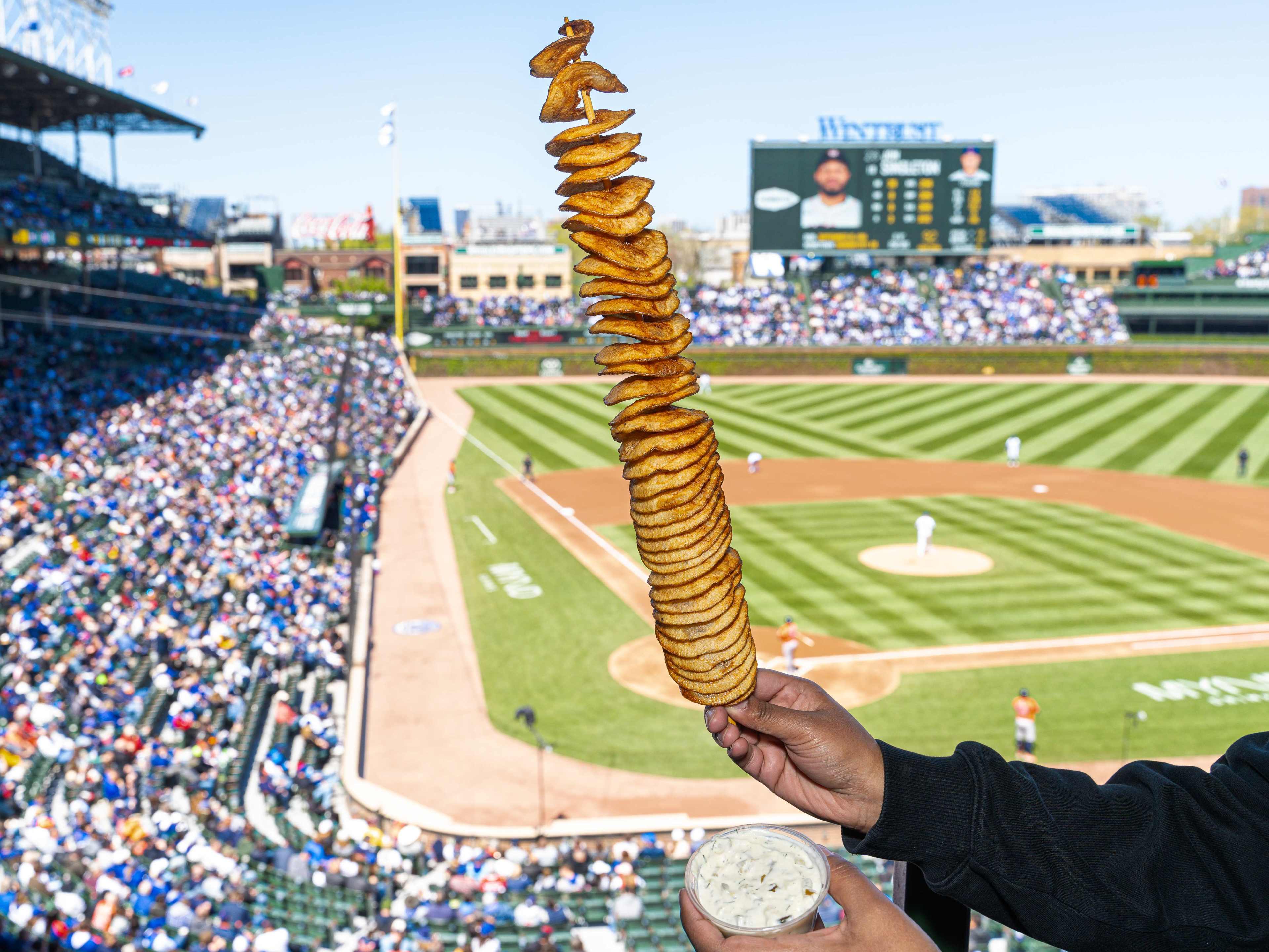 A footlong fried potato twist on a stick with a Cubs game in the background.