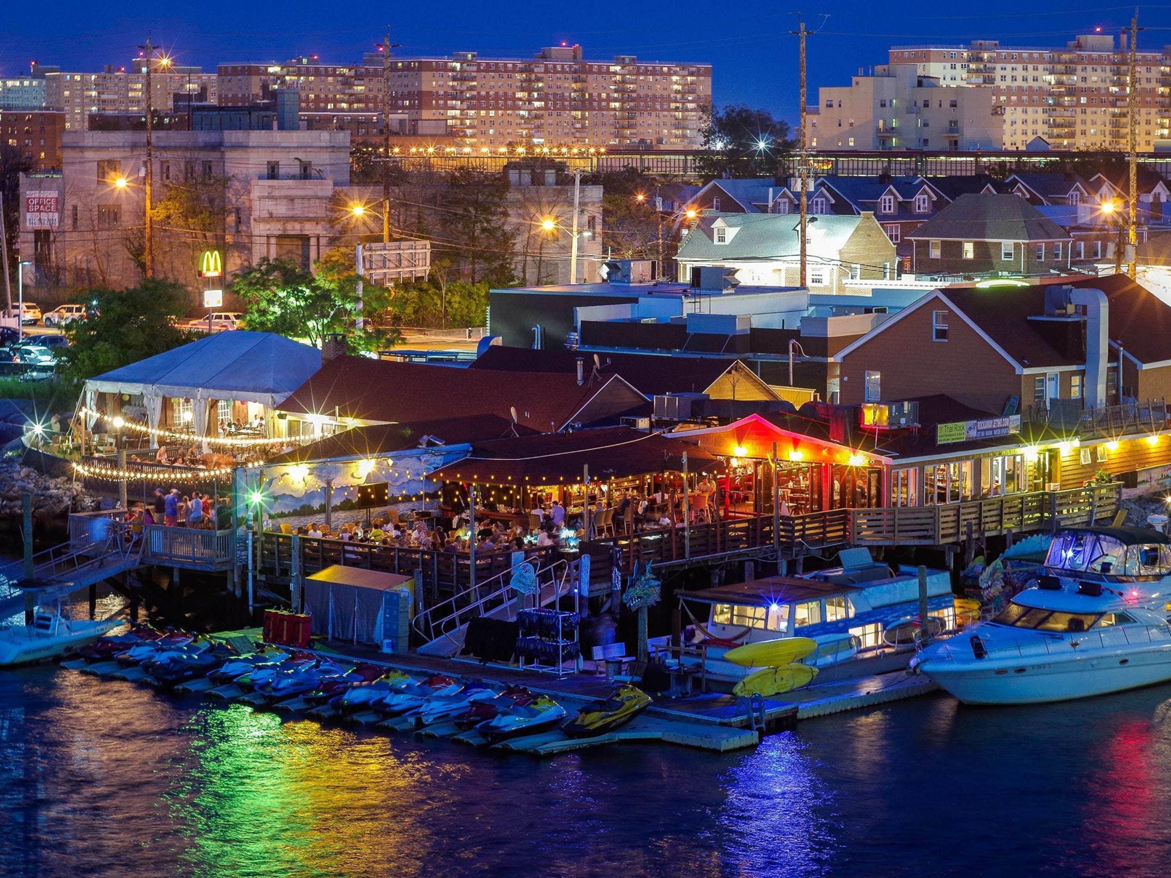 The exterior of Thai Rock at night lit by city lights and colorful hanging lights. Thai Rock is located right on the water.