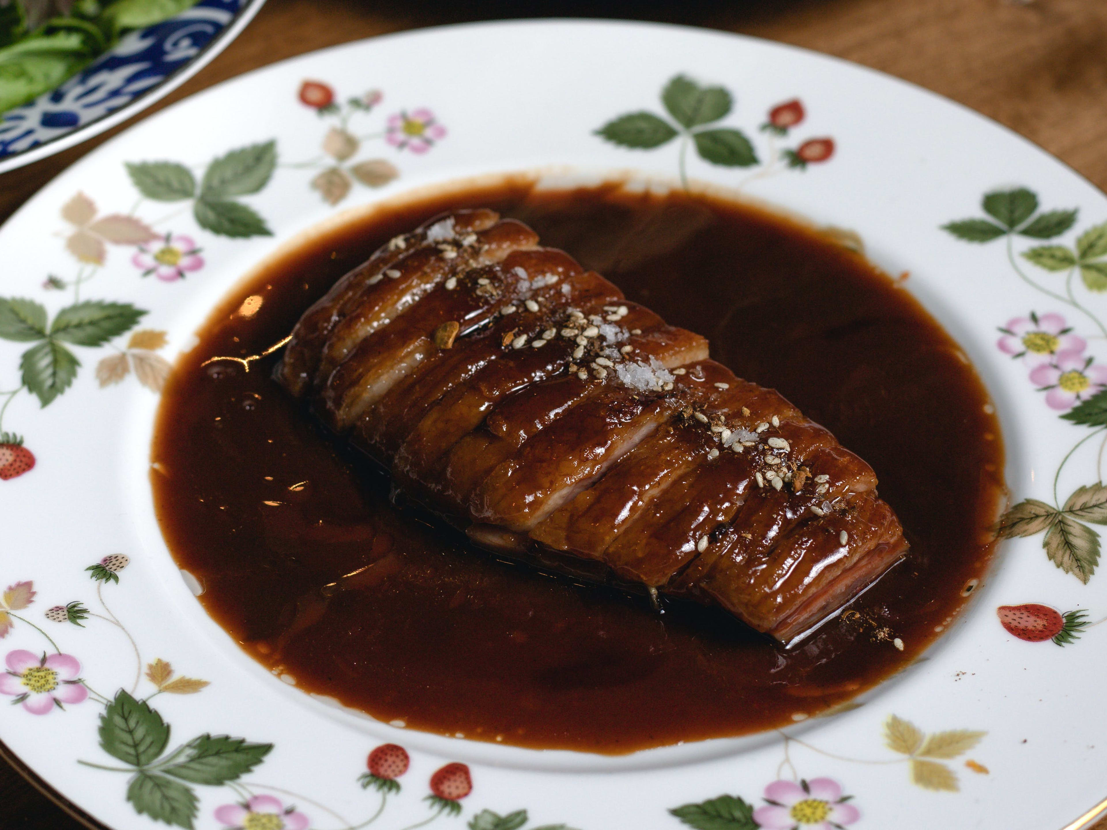 sliced duck in pool of sauce on decorative porcelain plate