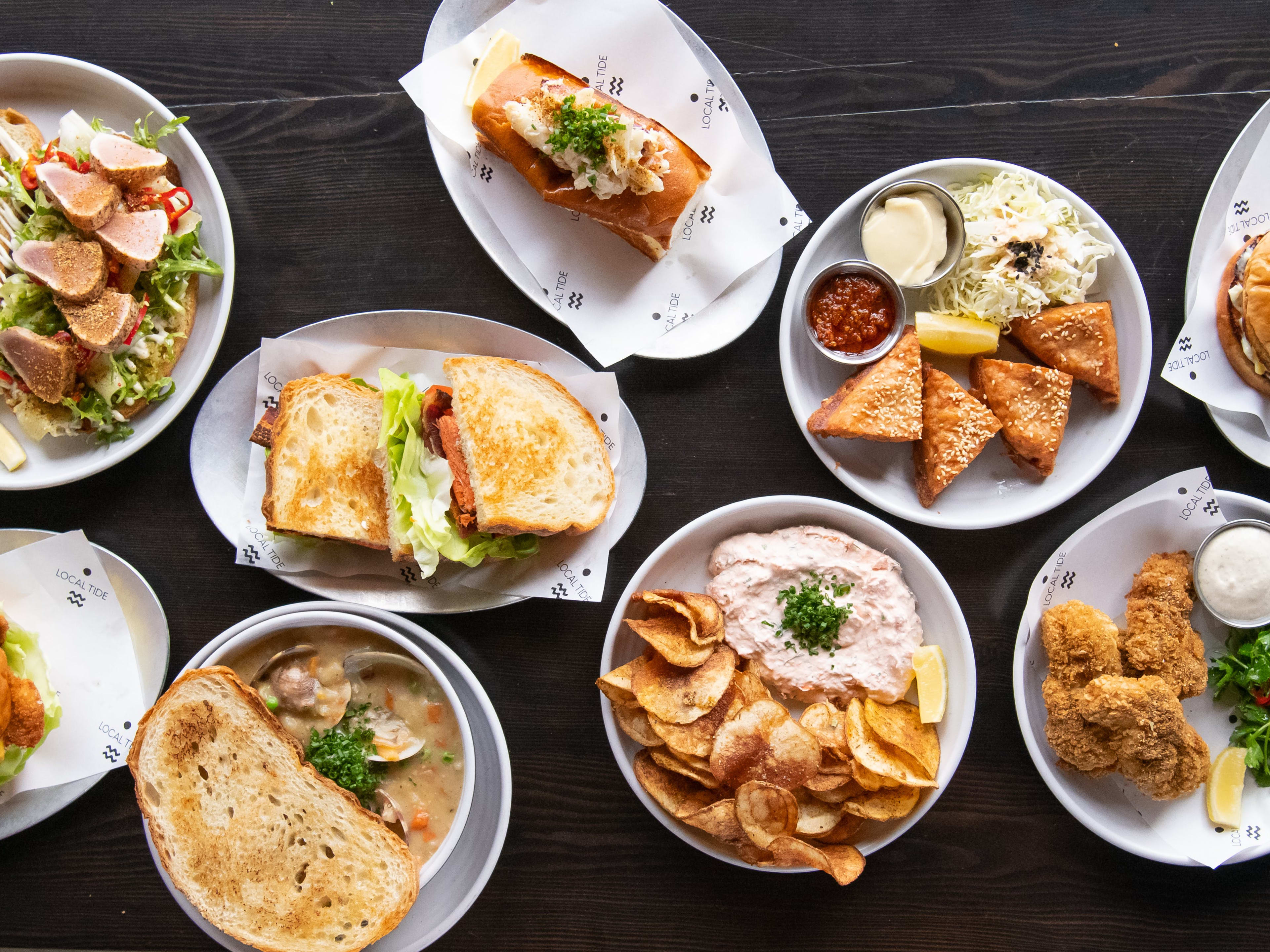 Spread of seafood dishes, like a crab roll, salmon BLT, shrimp toast, clam chowder, and fried nuggets of dover sole.