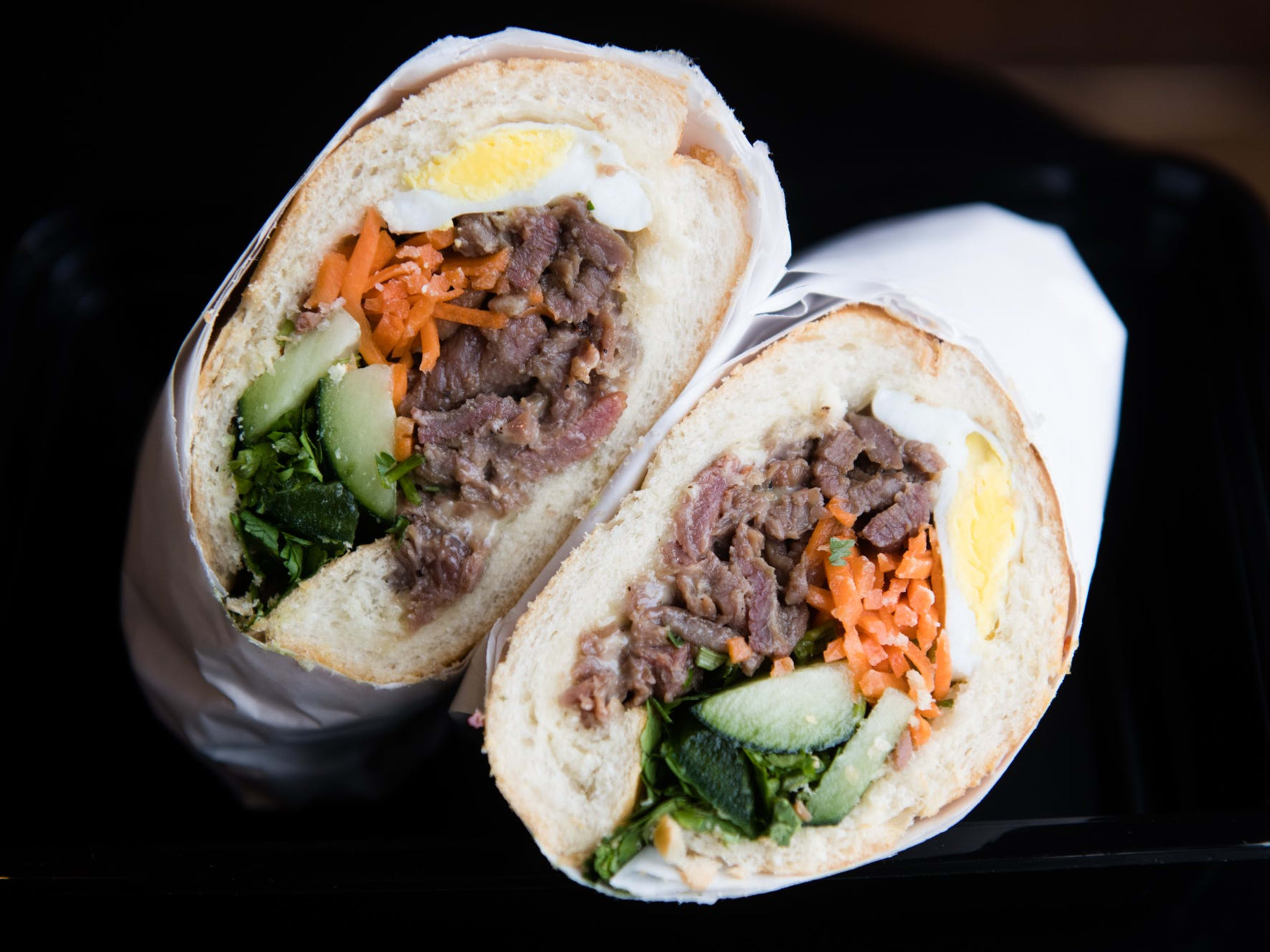 a banh mi with steak, pickled carrots, a fried egg, cucumber, and cilantro.