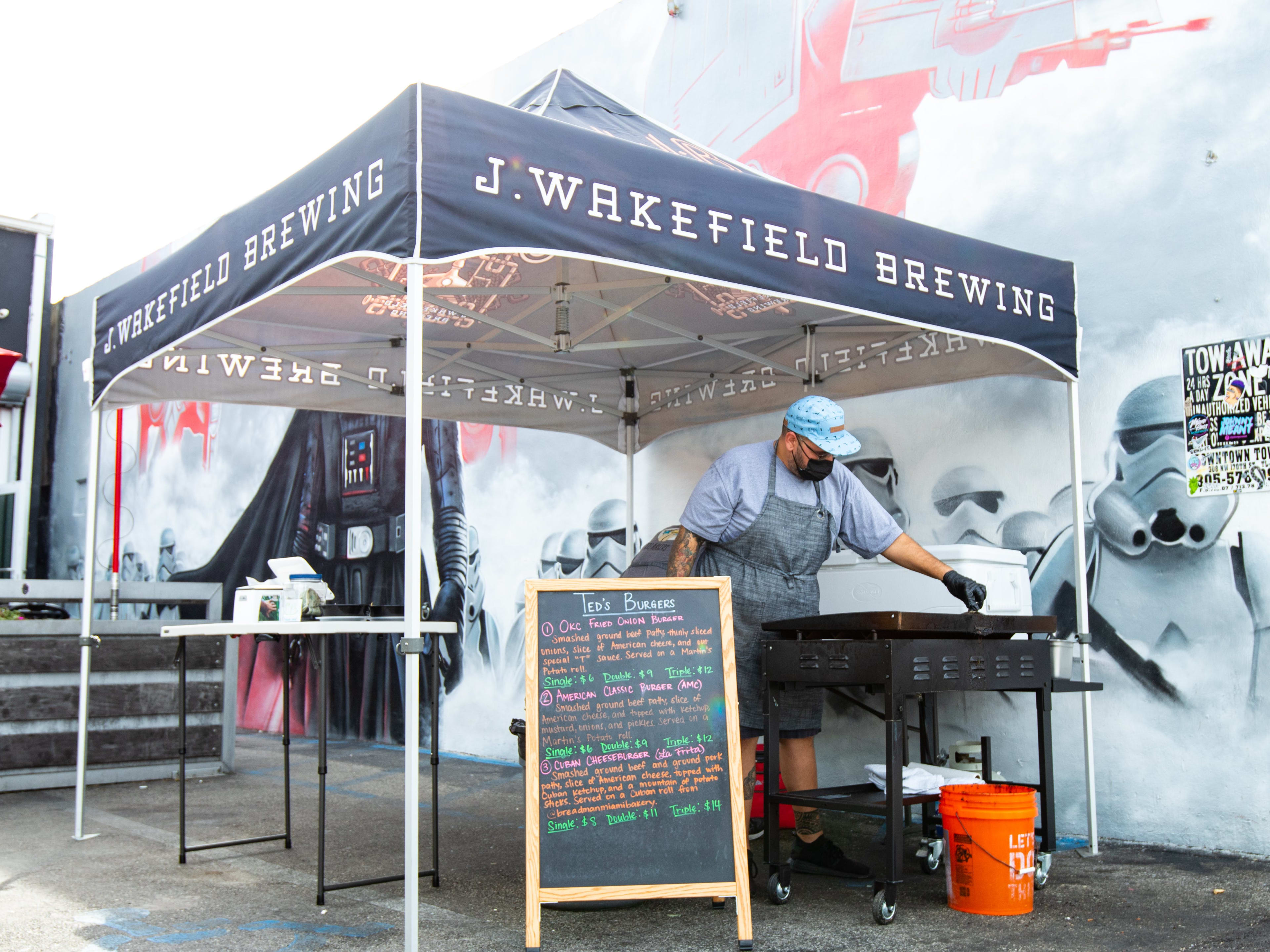 A man cooks burgers underneath a tent outside a brewery.